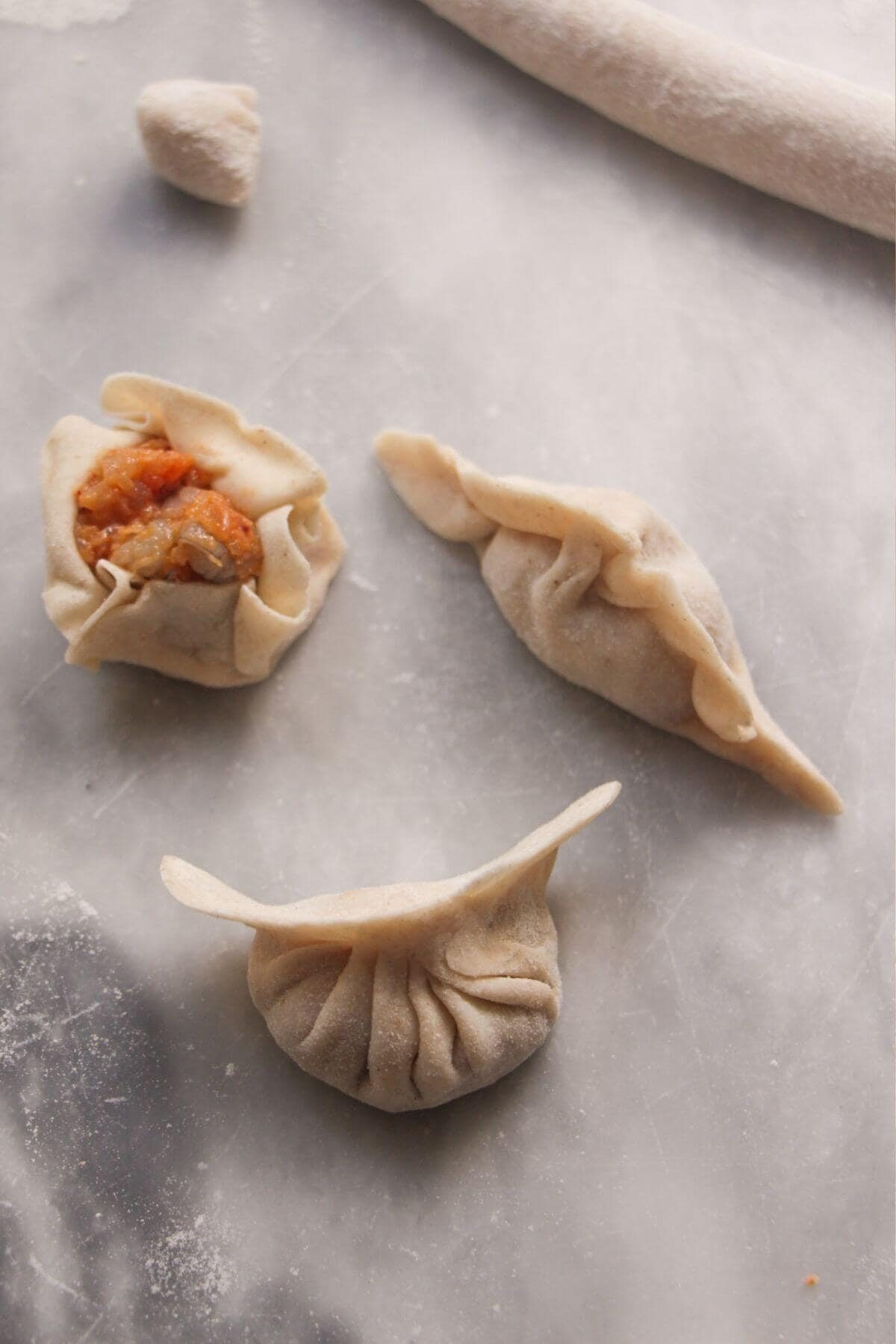 Three different styles of folded dumplings on a marble background.