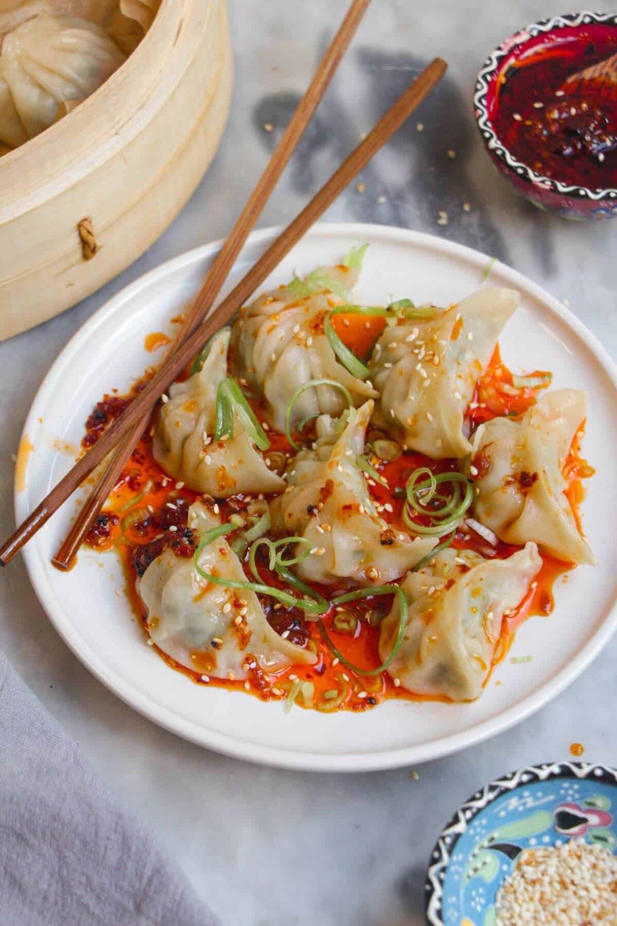 Steamed dumplings on a small white plate, drizzled with chilli oil.