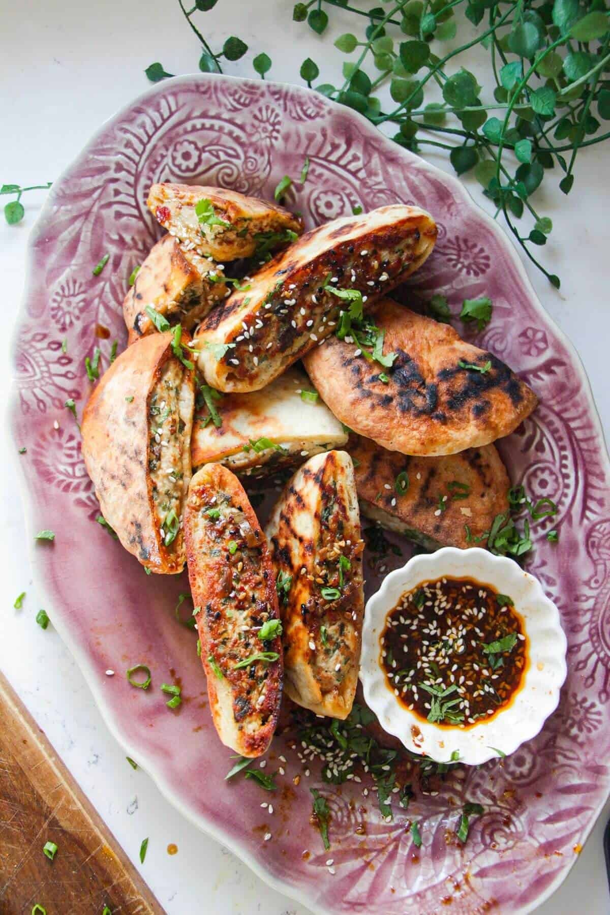 Dumpling stuffed flatbreads on a pink plate with dipping sauce on the side.