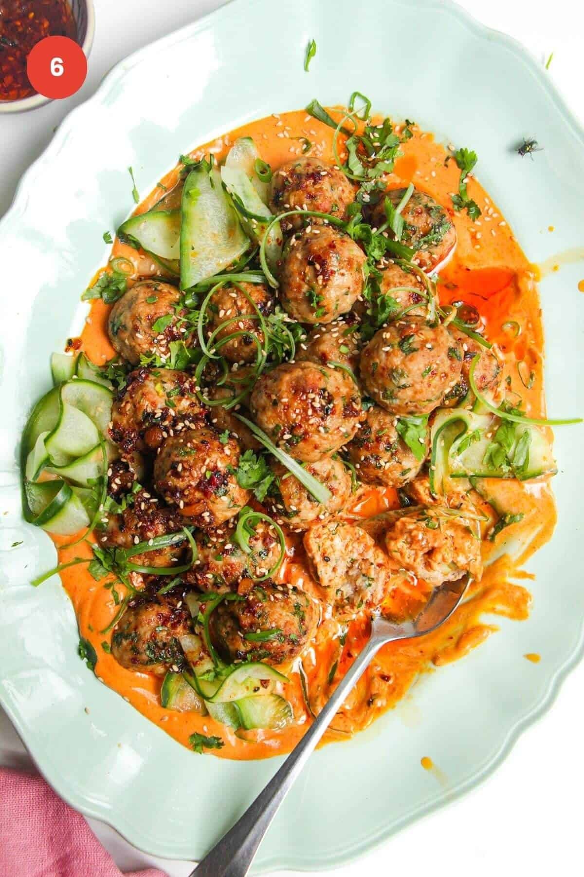 Dumpling meatballs on gochuajang sauce with pickled cucumber on an oval platter.