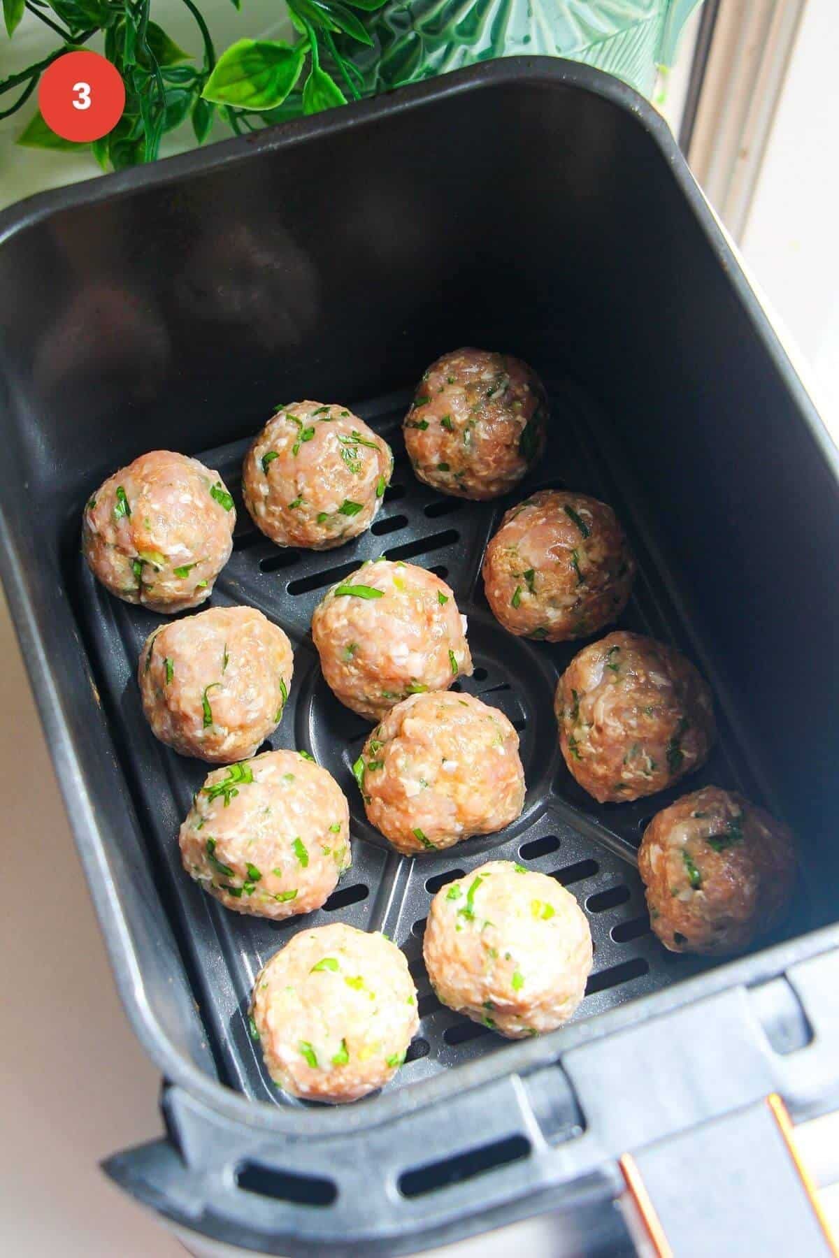Rolled dumpling meatballs in air fryer basket.