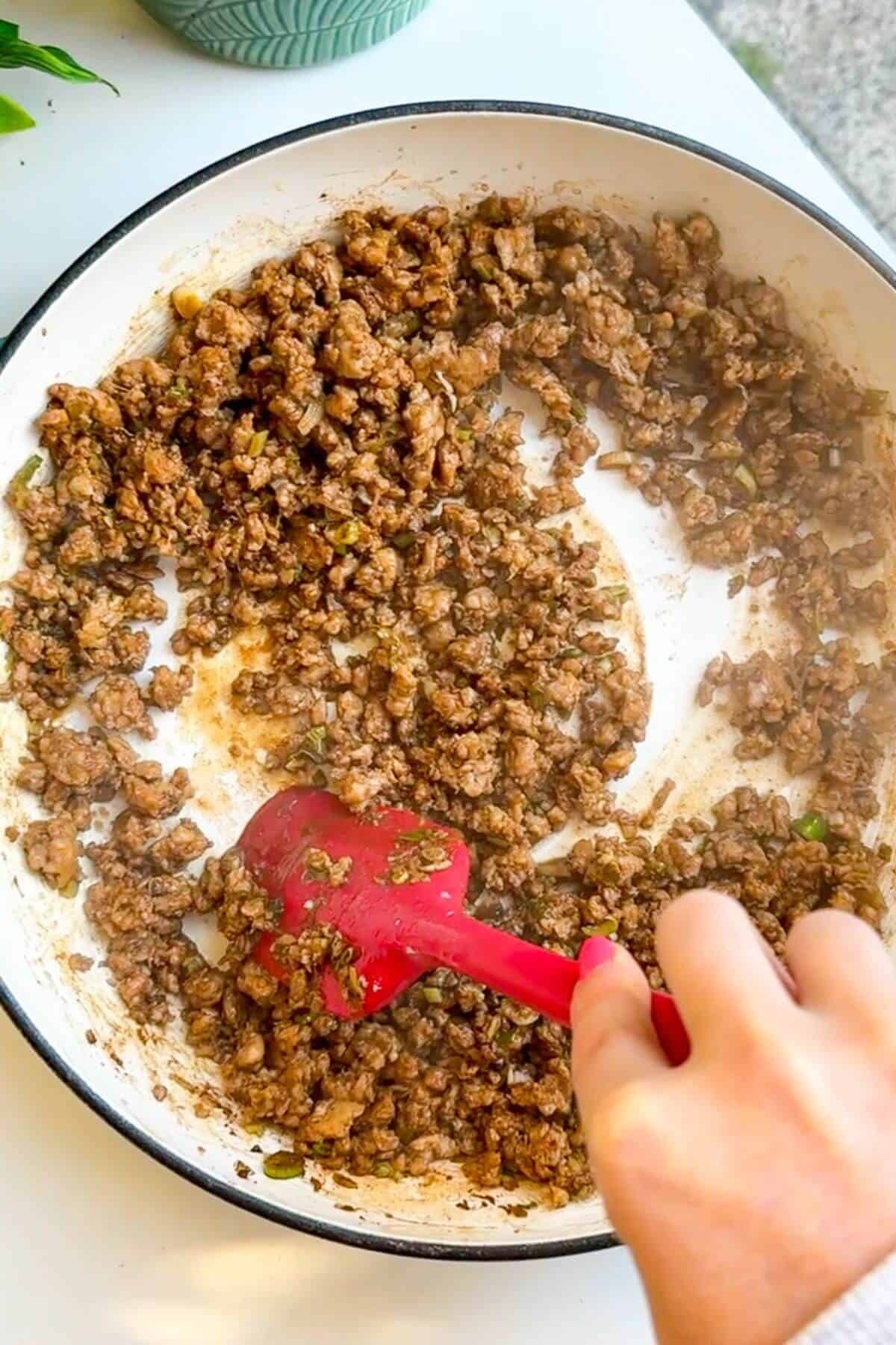 Spatula stirring browned ground chicken in a pan.