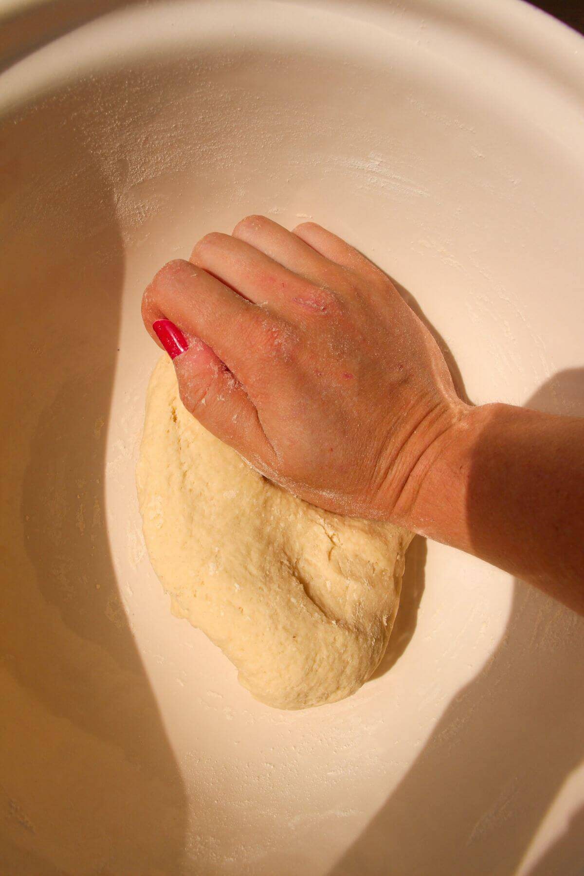 Hand kneading dumpling dough in a large white bowl.