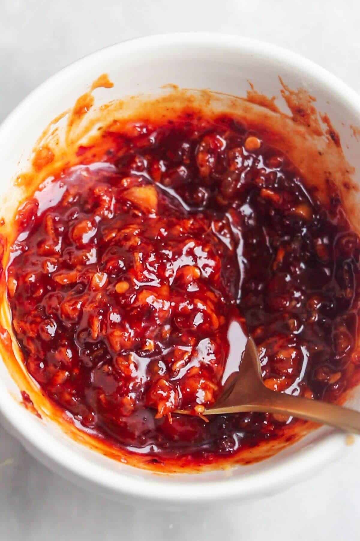 Honey and harissa being mixed with a small gold spoon in a white bowl.