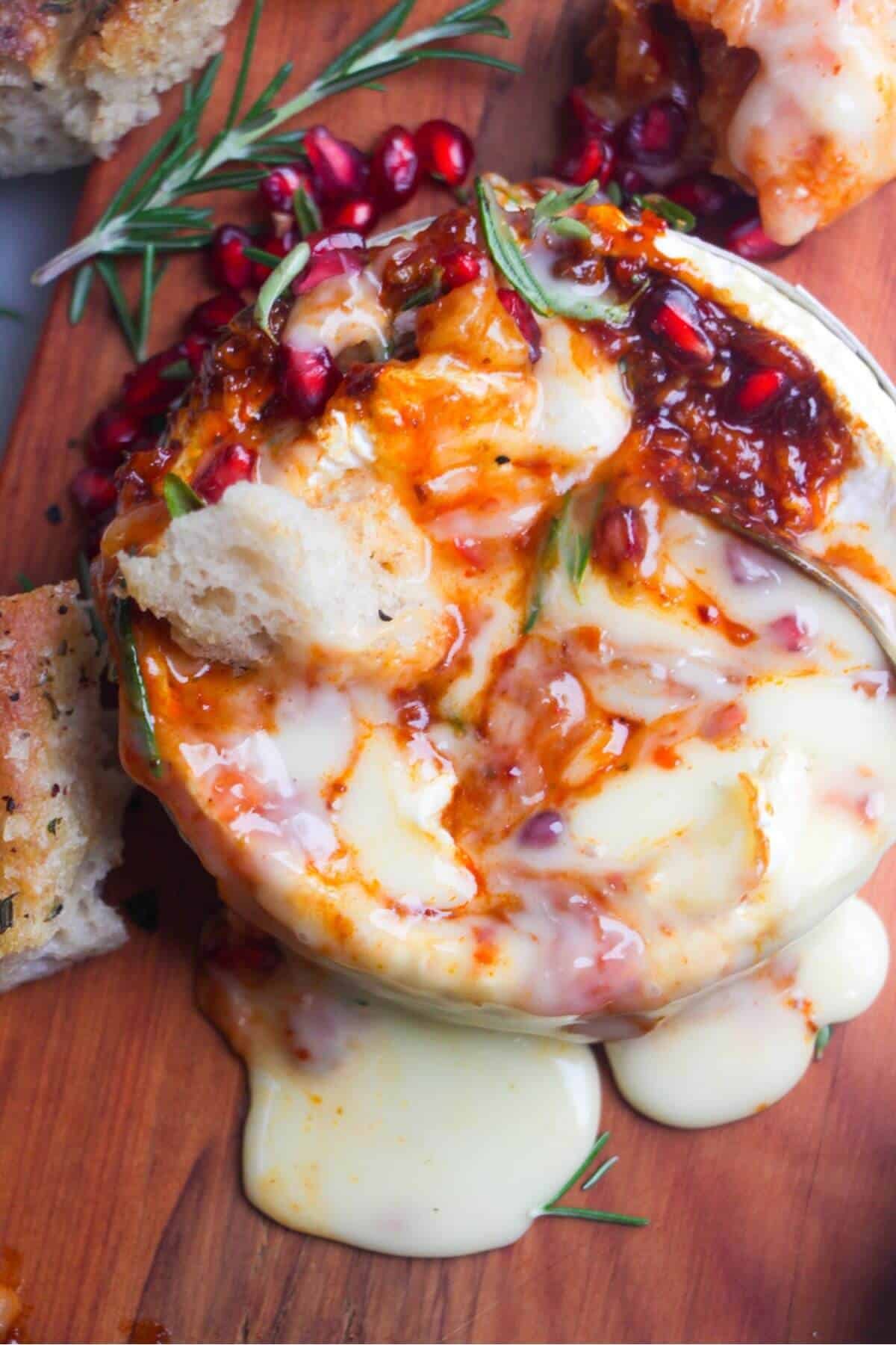 Gooey, melty cheese pooling out of a wheel of camembert onto a small wooden board, with pieces of focaccia on the side.