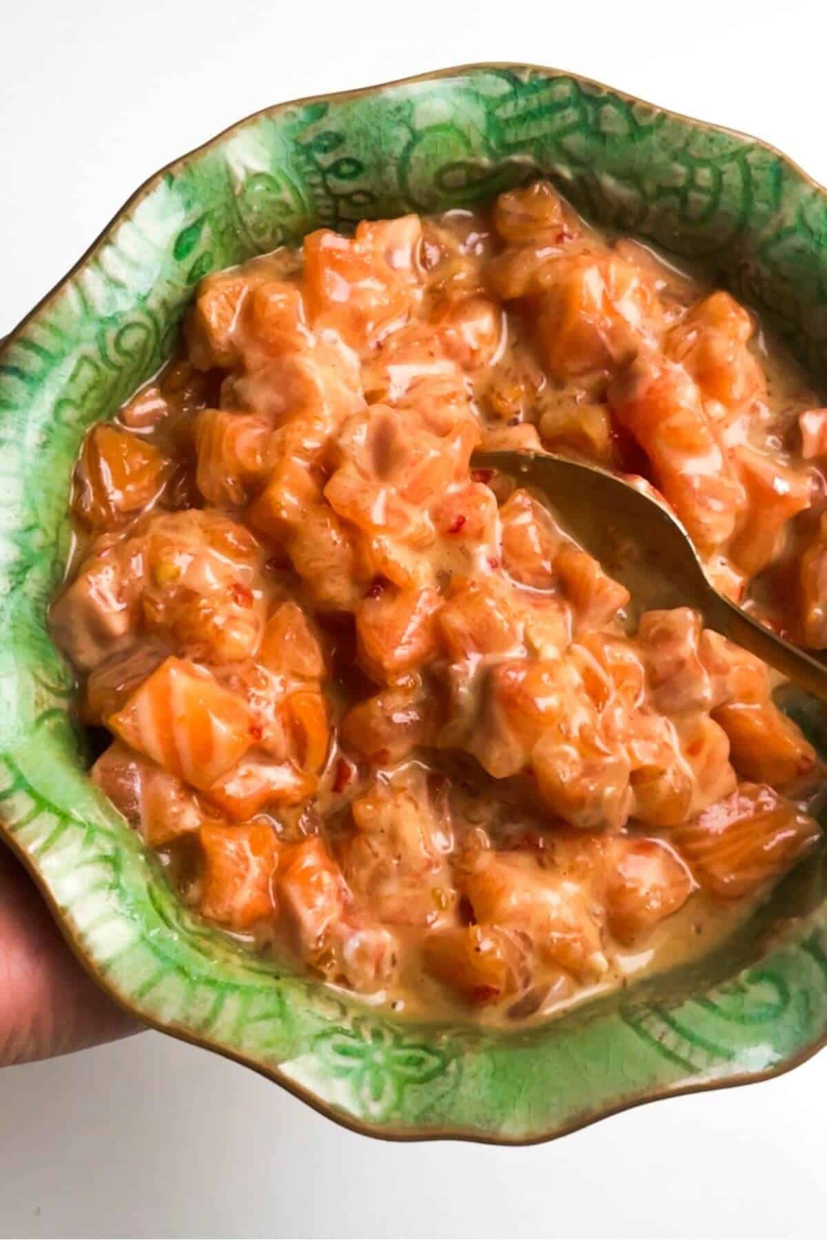 Diced salmon mixed with seasoning in a small green bowl.