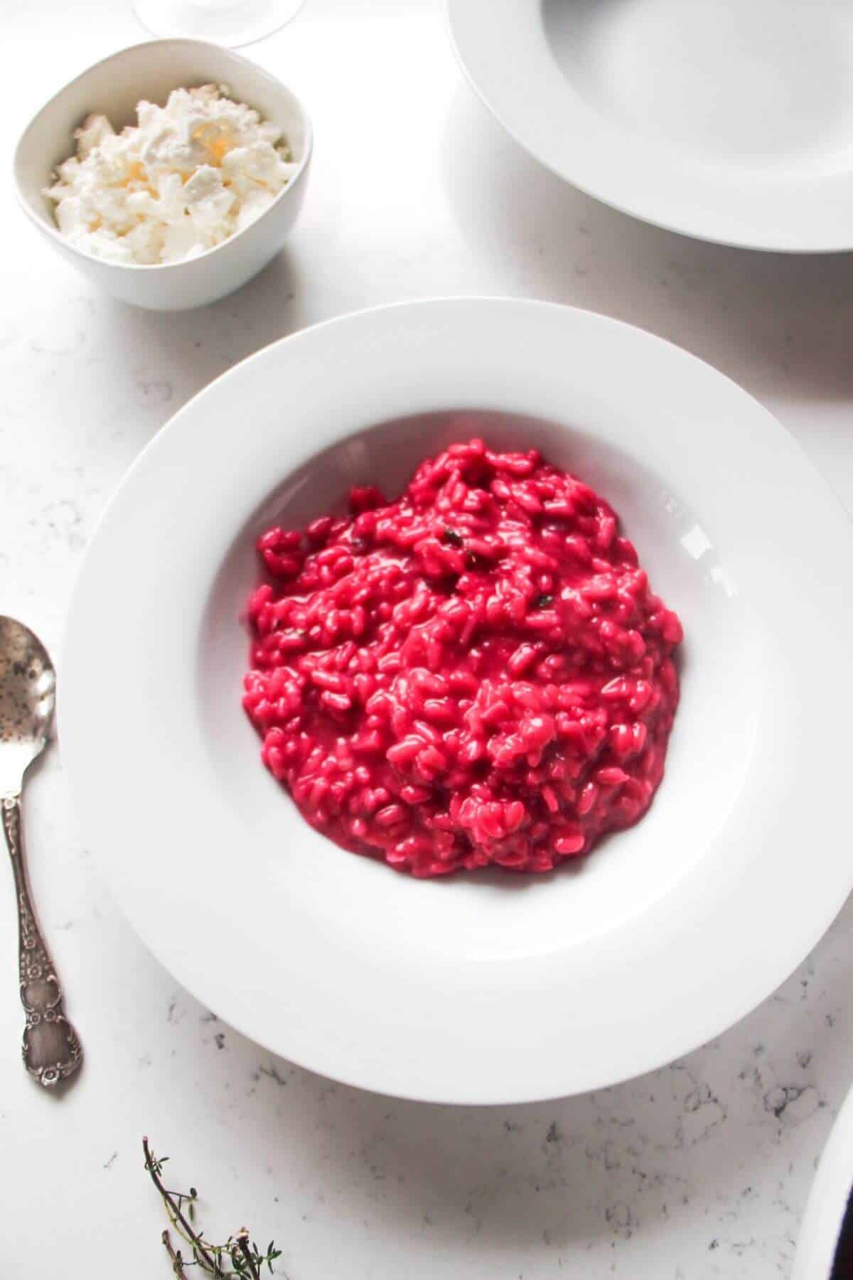 Bright pink beetroot risotto in a small white bowl with feta on the side.