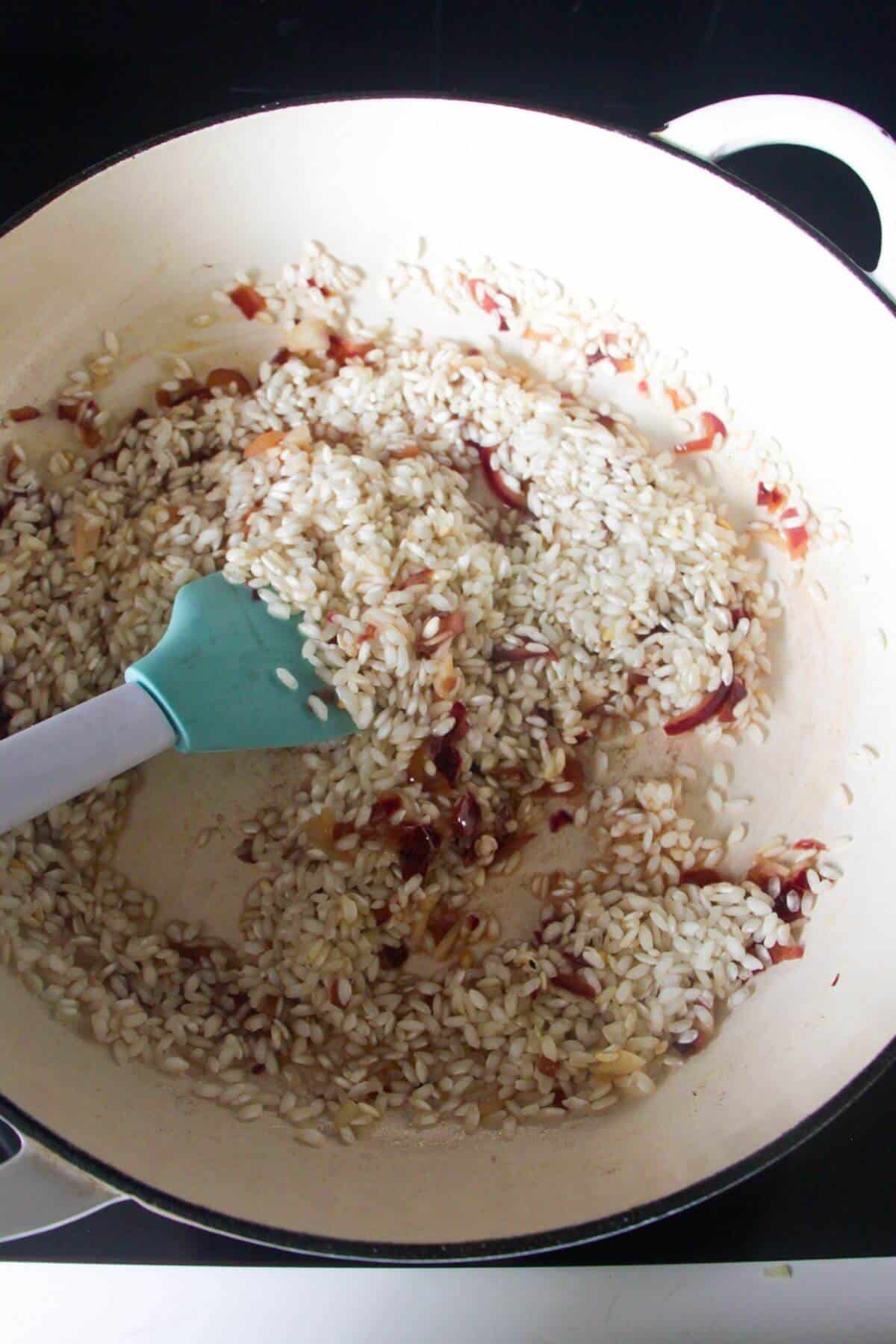 Blue and white spatula stirring stock through rice in a white skillet.