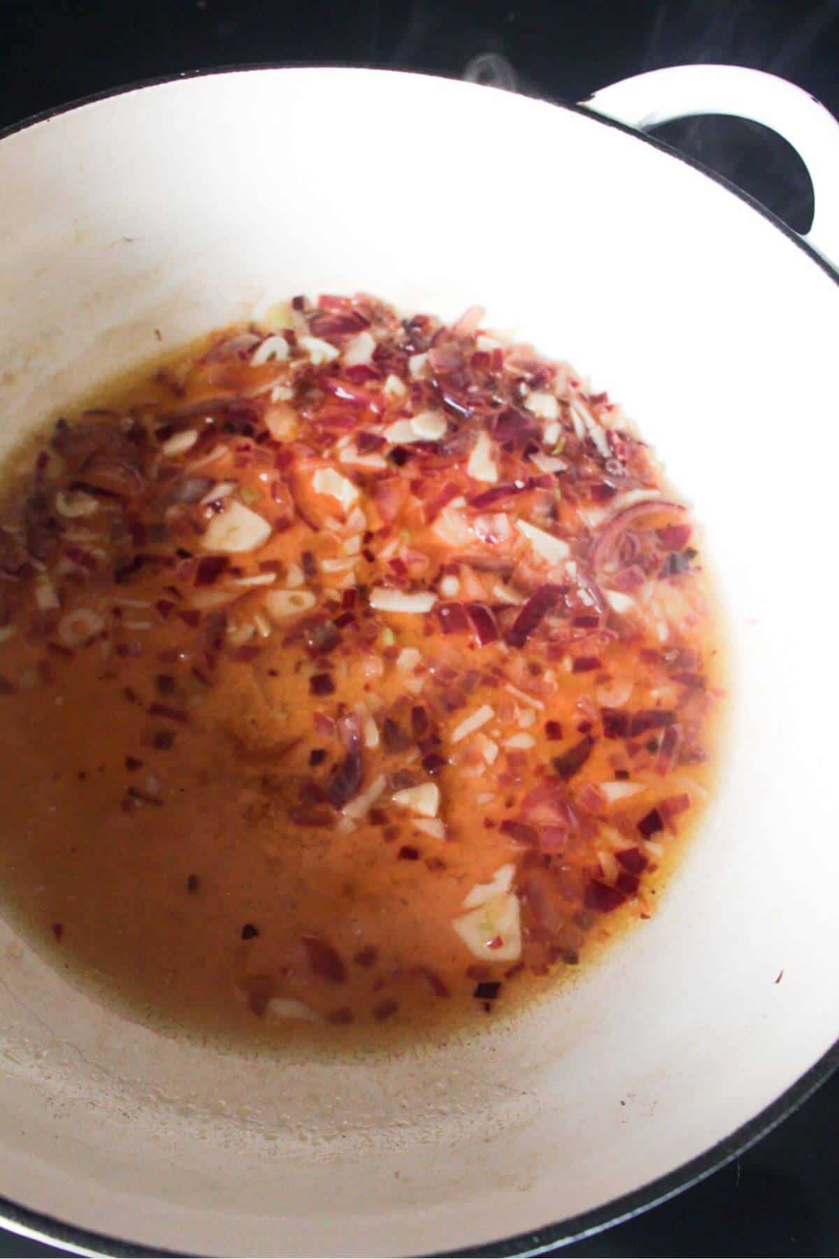 Onions and garlic cooking in a large white skillet with white wine.