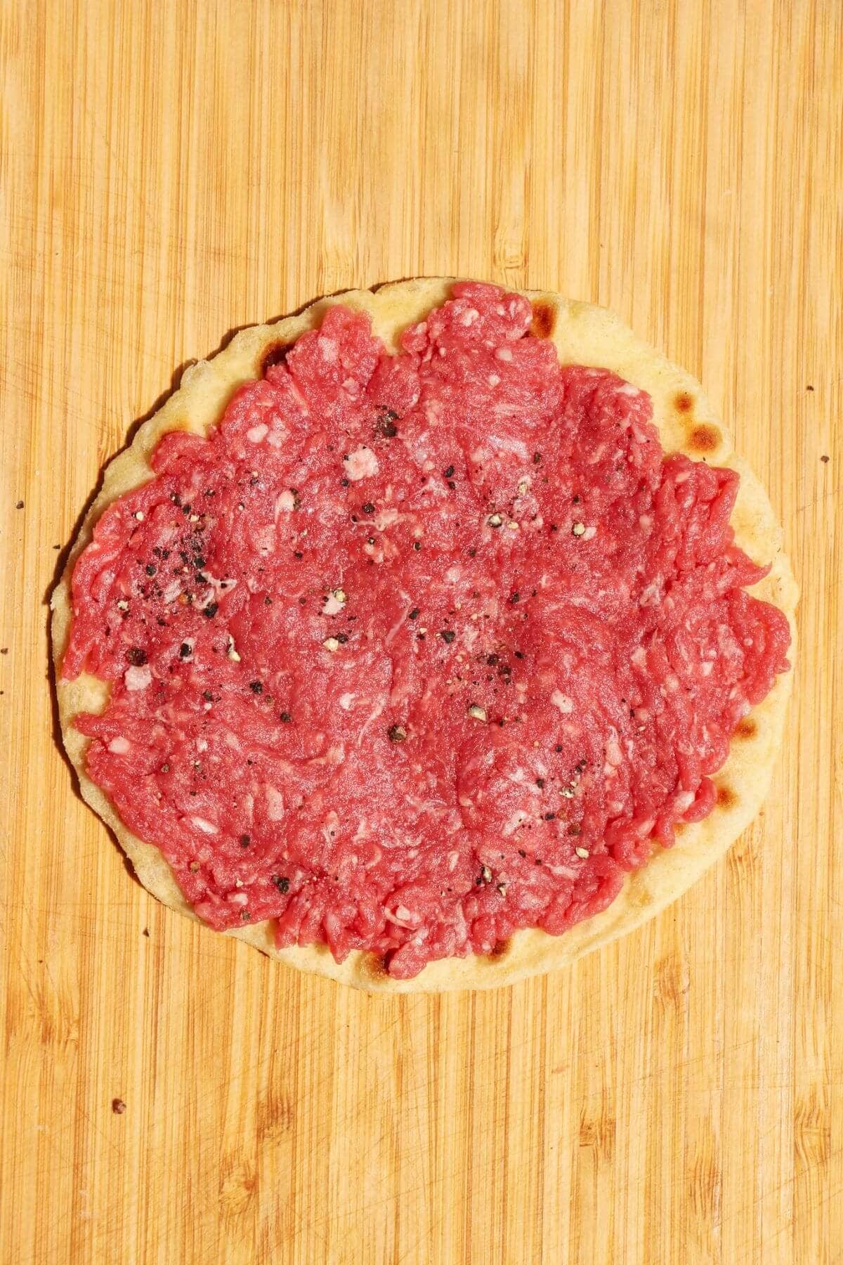 Ground beef pressed into small flour tortilla on a wooden background.