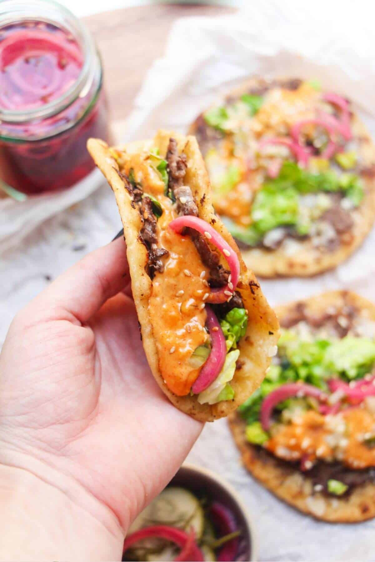 Hand holding up a Big Mac taco with more tacos in the background.