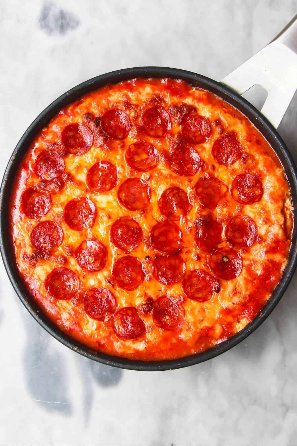 Melted cheese and charred pepperoni in a small black pan.