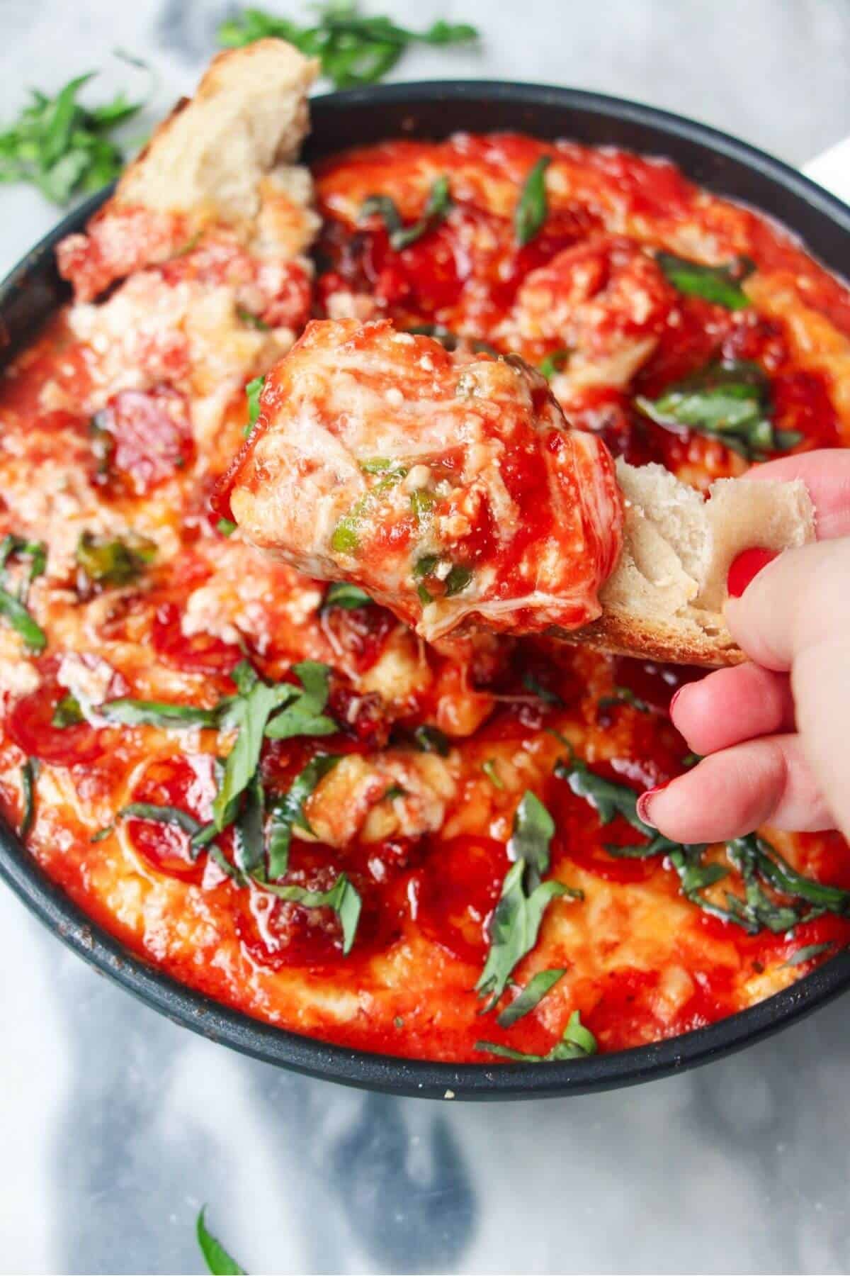 Cheesy pizza dip on a piece of bread with the rest of the pizza dip in the background.