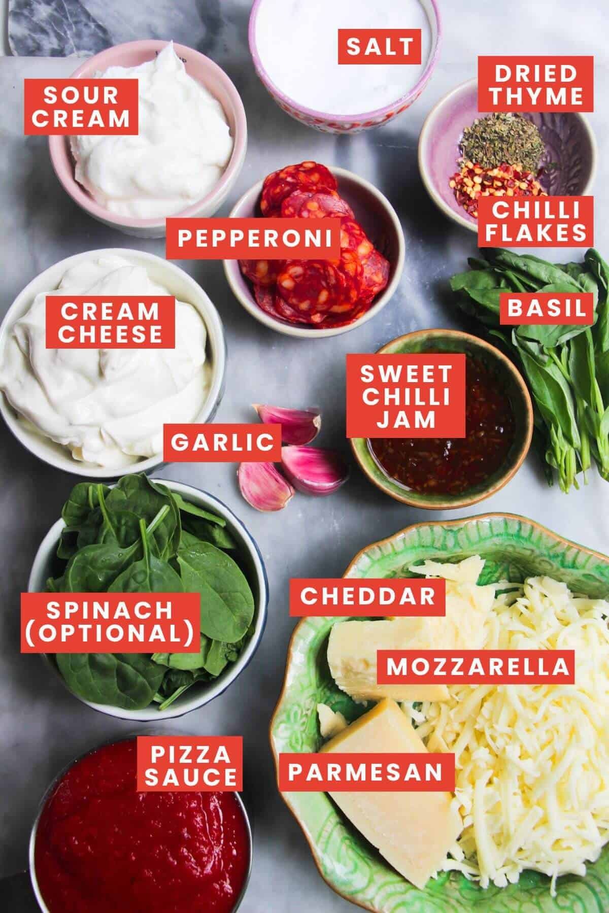 Ingredients for cheesy pizza dip laid out on a grey marble background and labelled.