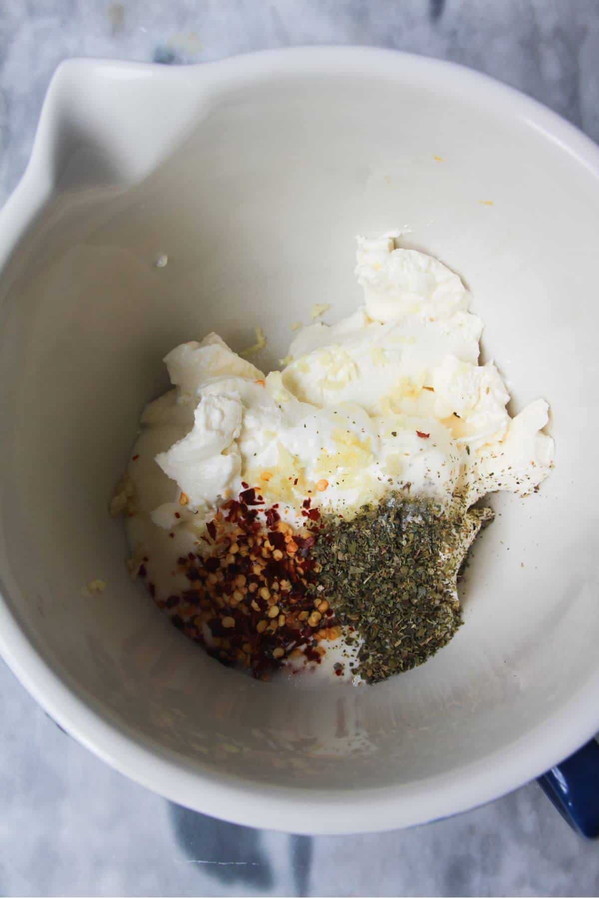 Cream cheese, sour cream, dried herb, chilli flakes and garlic in a small white mixing bowl.