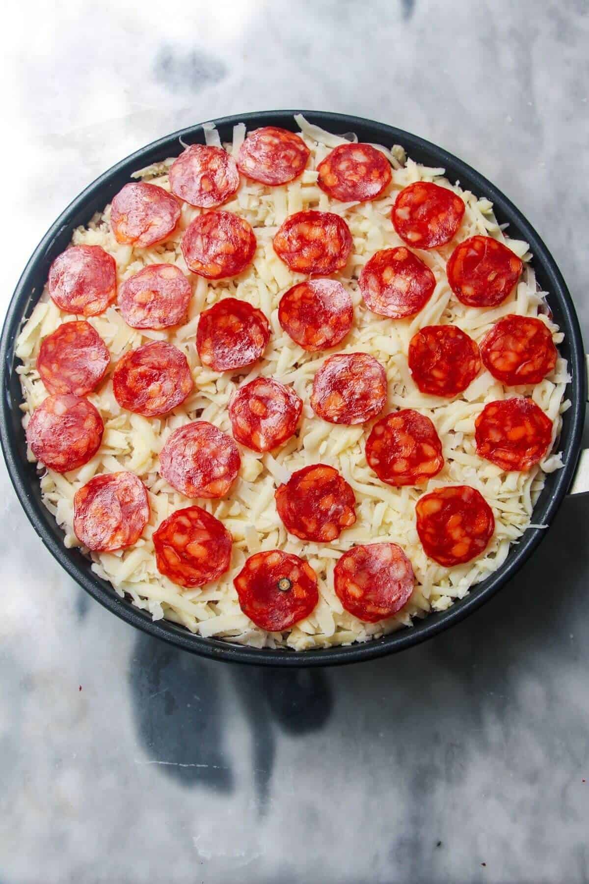 Pepperoni and grated cheese in a small black pan.