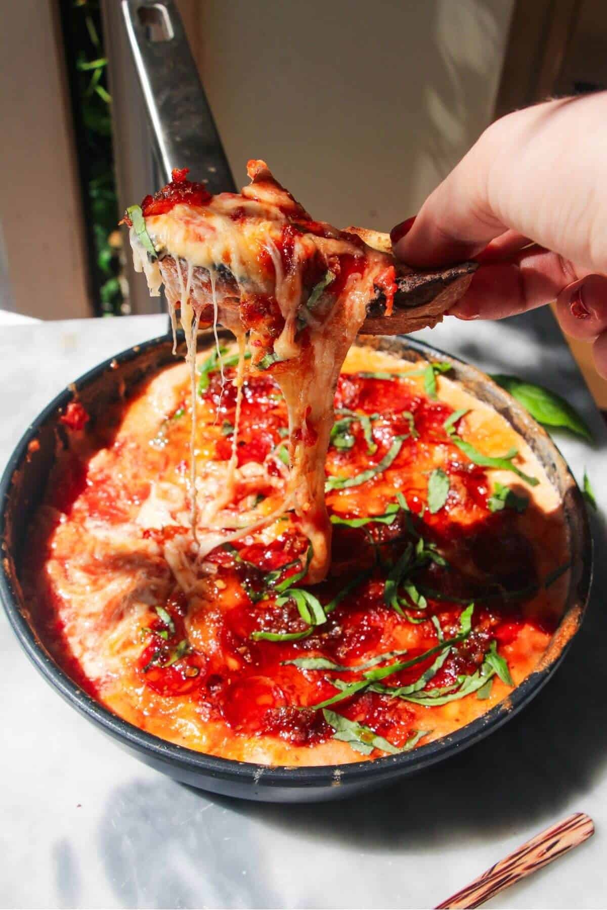 Hand pulling up a piece of bread with cheesy pizza dip on it.