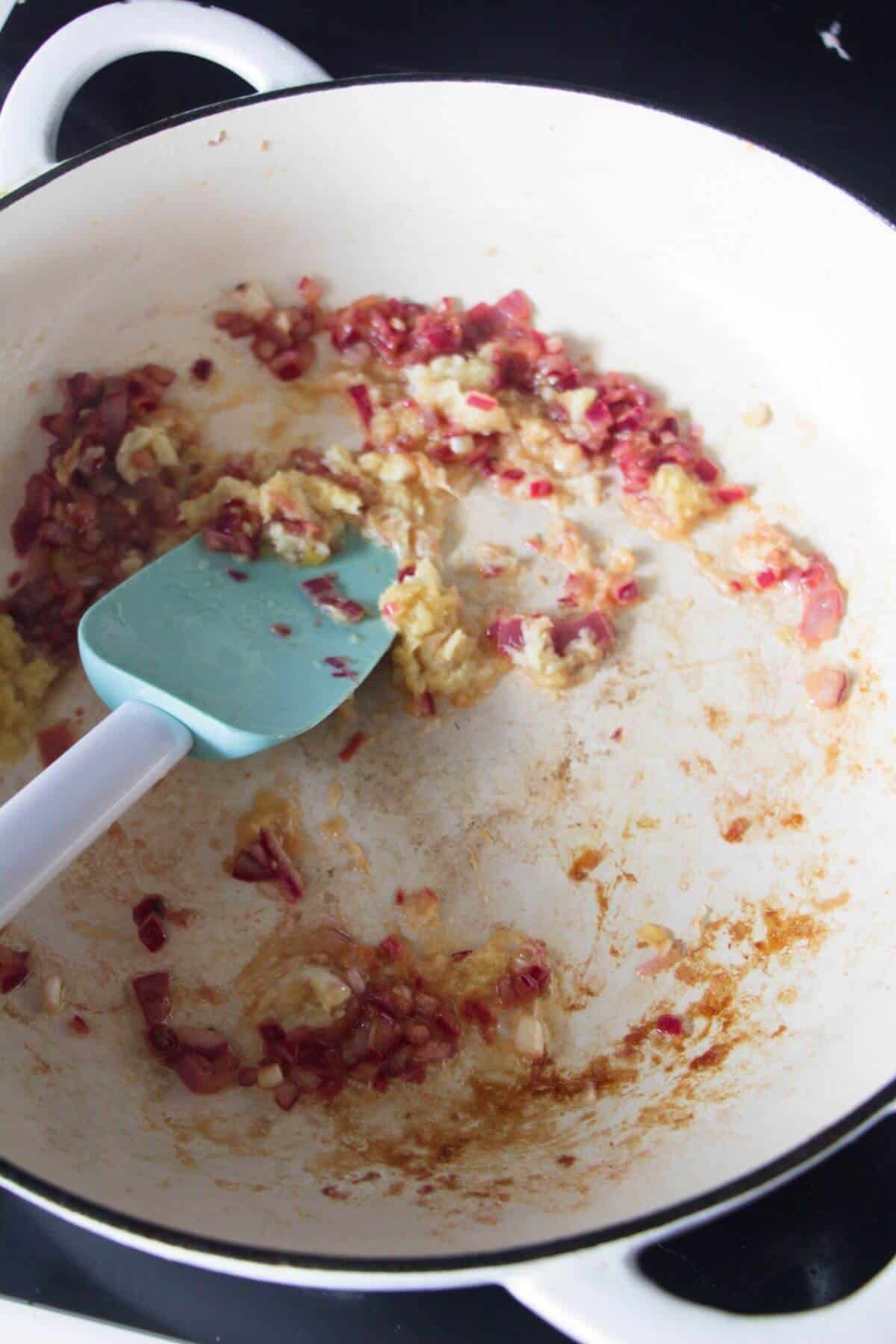 Diced onion and ginger being stirred in a large white skillet on the stove top.