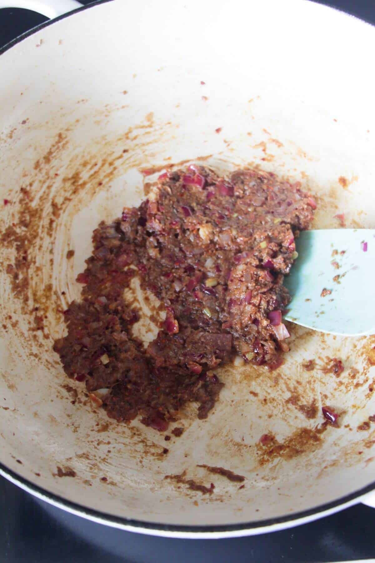 Saag spice paste being stirred in a large white skillet on the stove top.