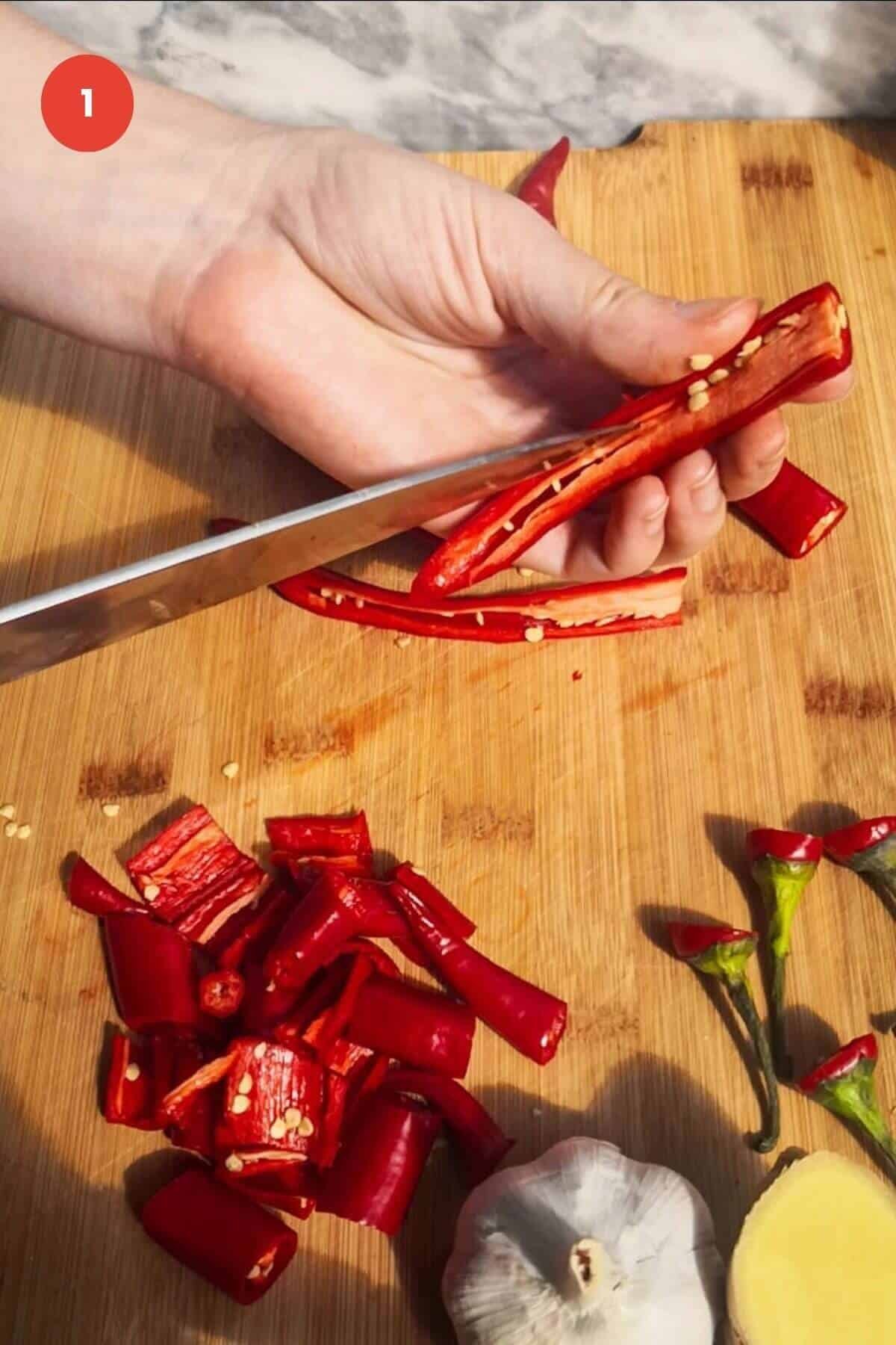 Slicing red chilies on chopping board.