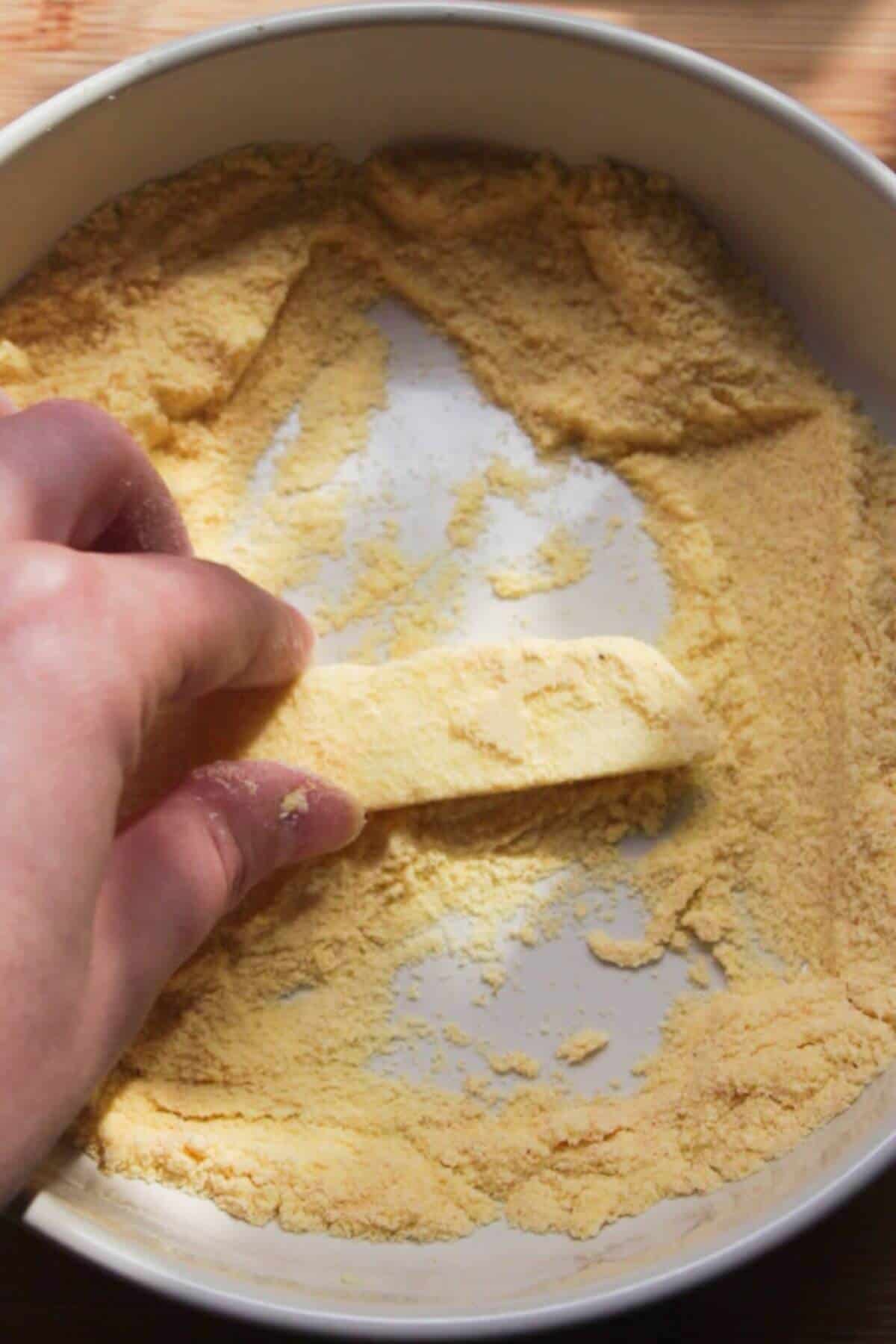 Hand coating a piece of halloumi in polenta in a small white bowl.
