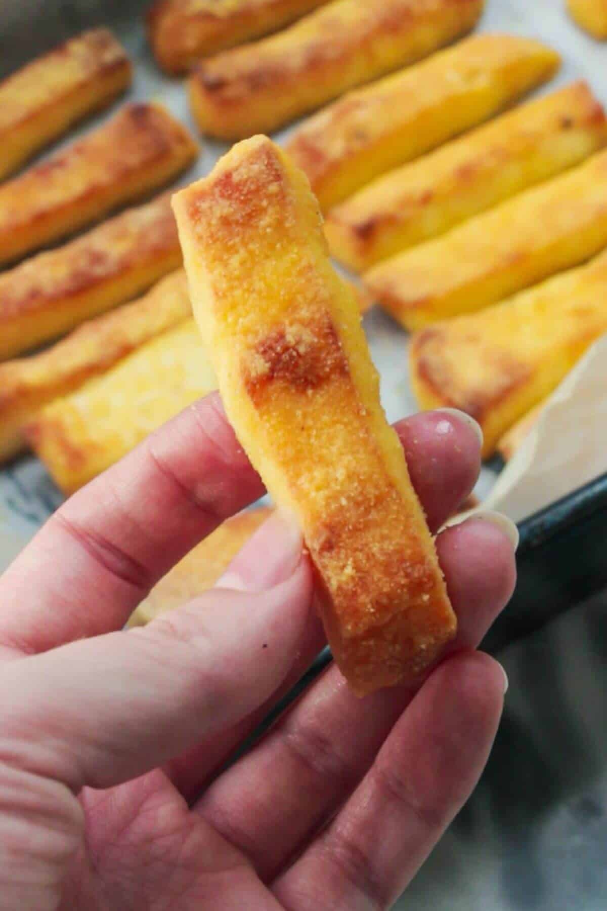 Close up of a hand holding up a crispy halloumi fry.