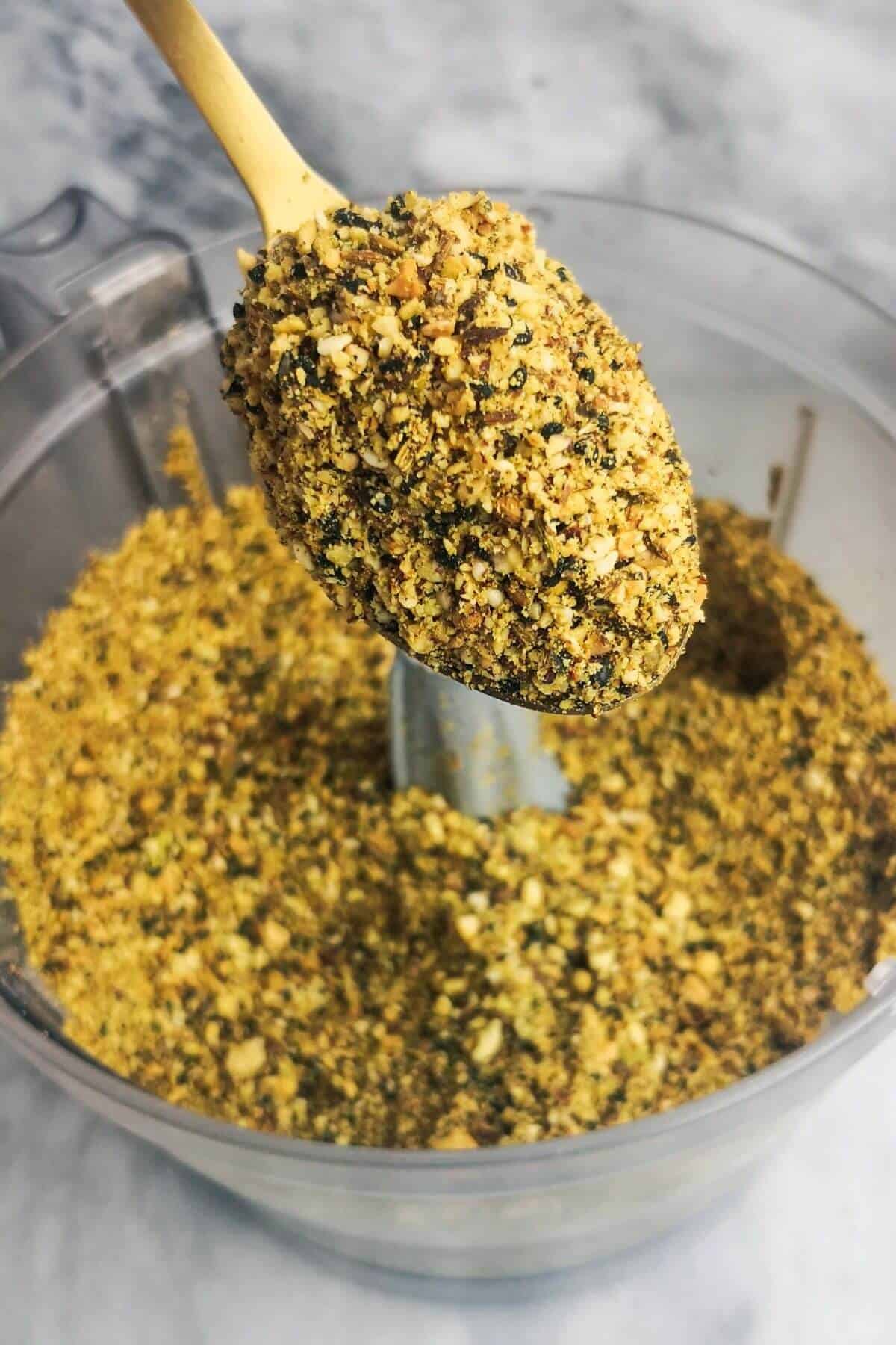 Close up of blitzed dukkah on a gold spoon with food processor bowl in the background.