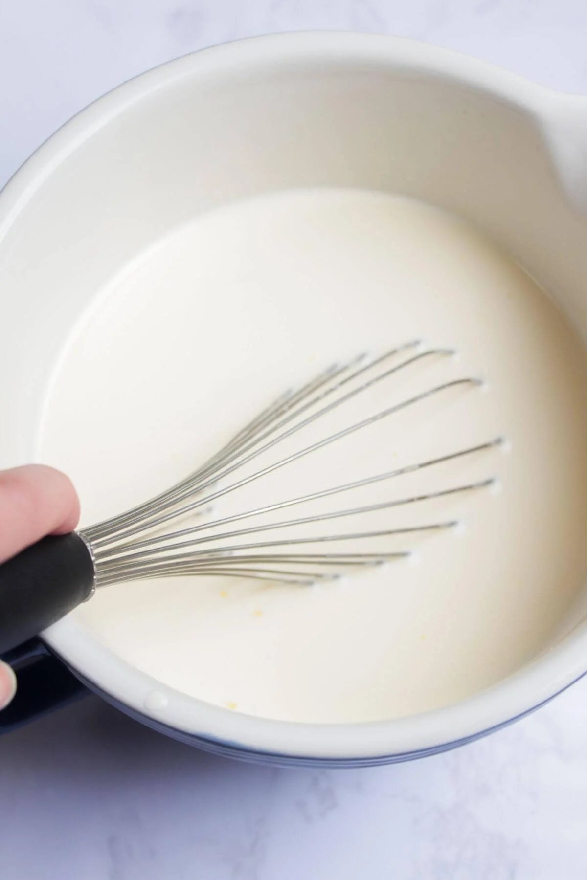 Whisking milk, cream, sugar and eggs together in a large white bowl.