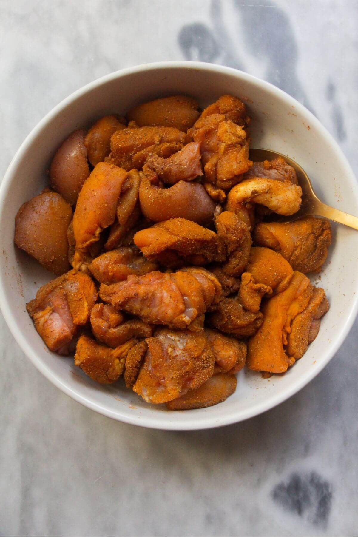 White bowl of chopped chicken tossed in spices with a gold spoon in the bowl.