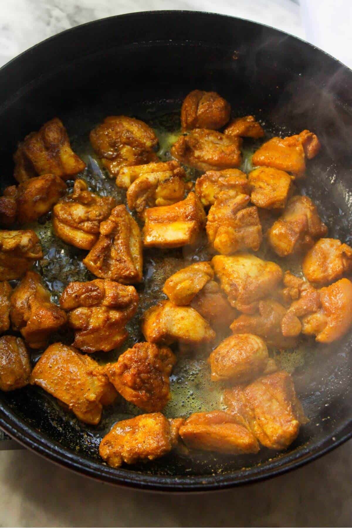 Browned and part-cooked chopped thighs in a large black pan.