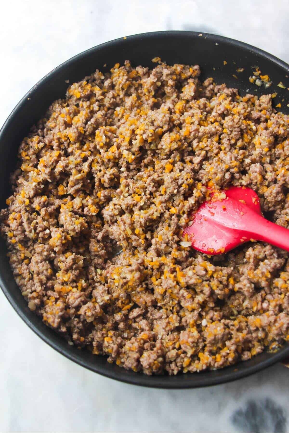 Red spatula stirring ground beef in a black skillet.