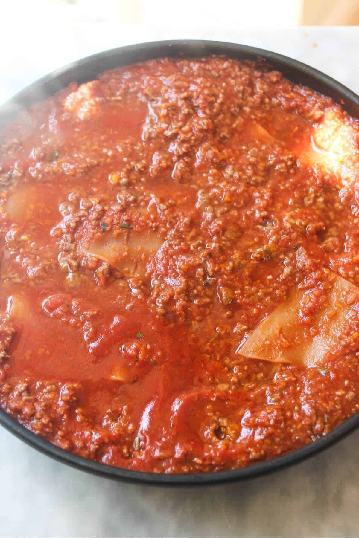 Lasagna sheet cooked in bolognese sauce in a small black pan.
