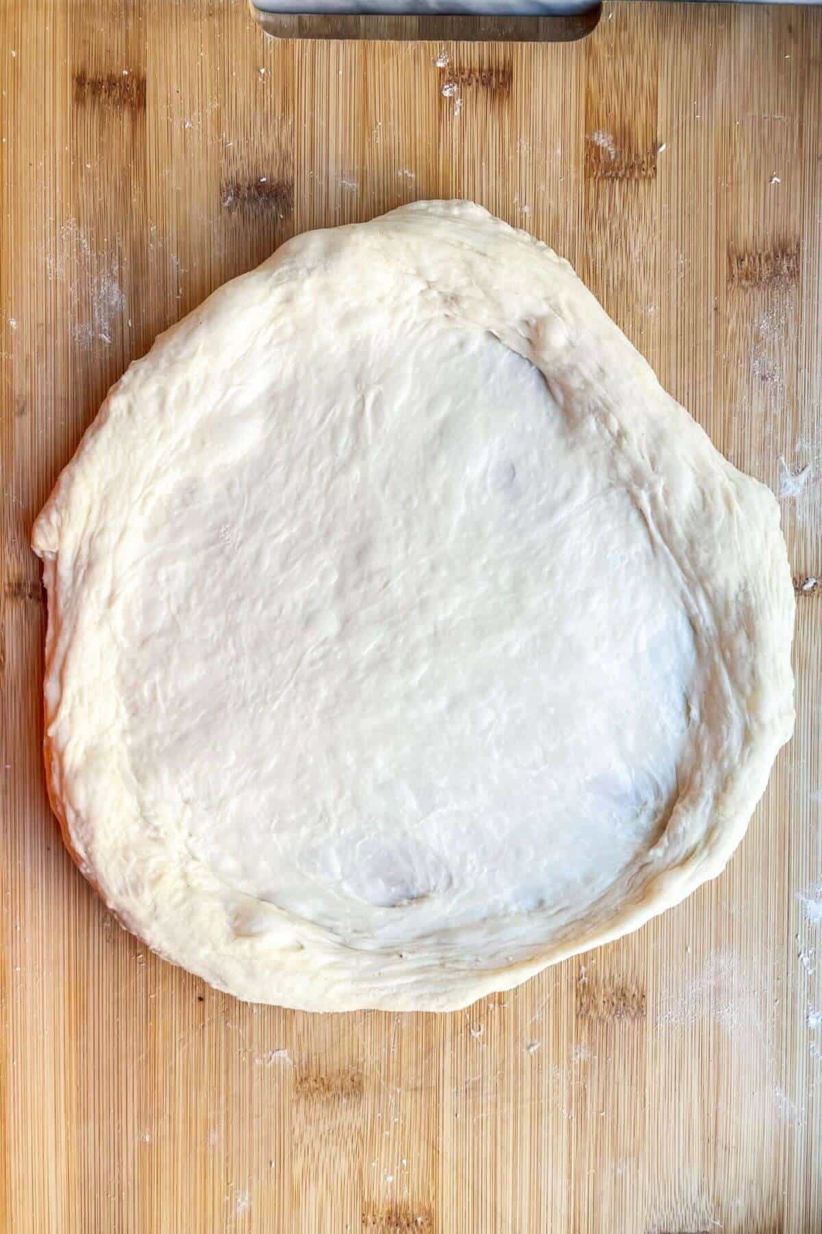 Pizza dough base on a wooden board ready to be topped.