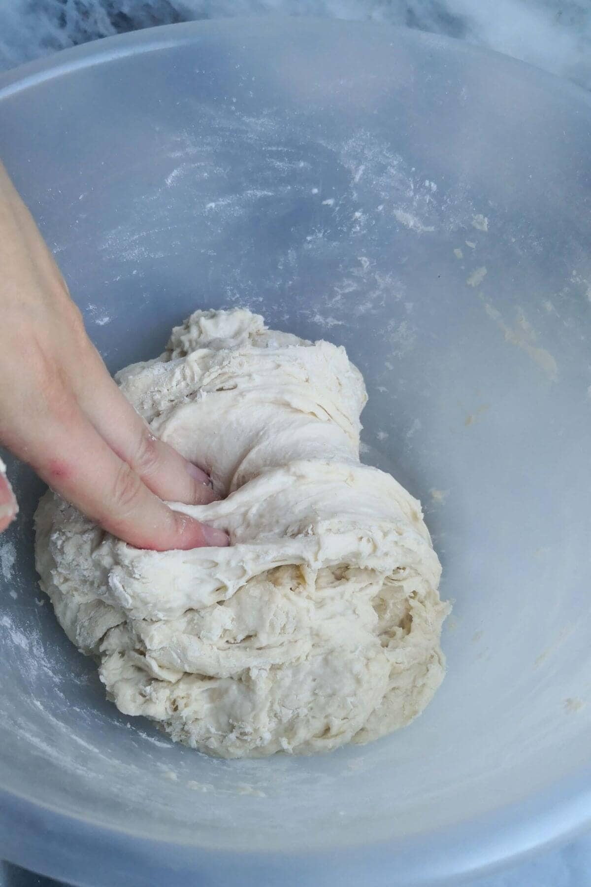Hand folding down dough in a clear mixing bowl.