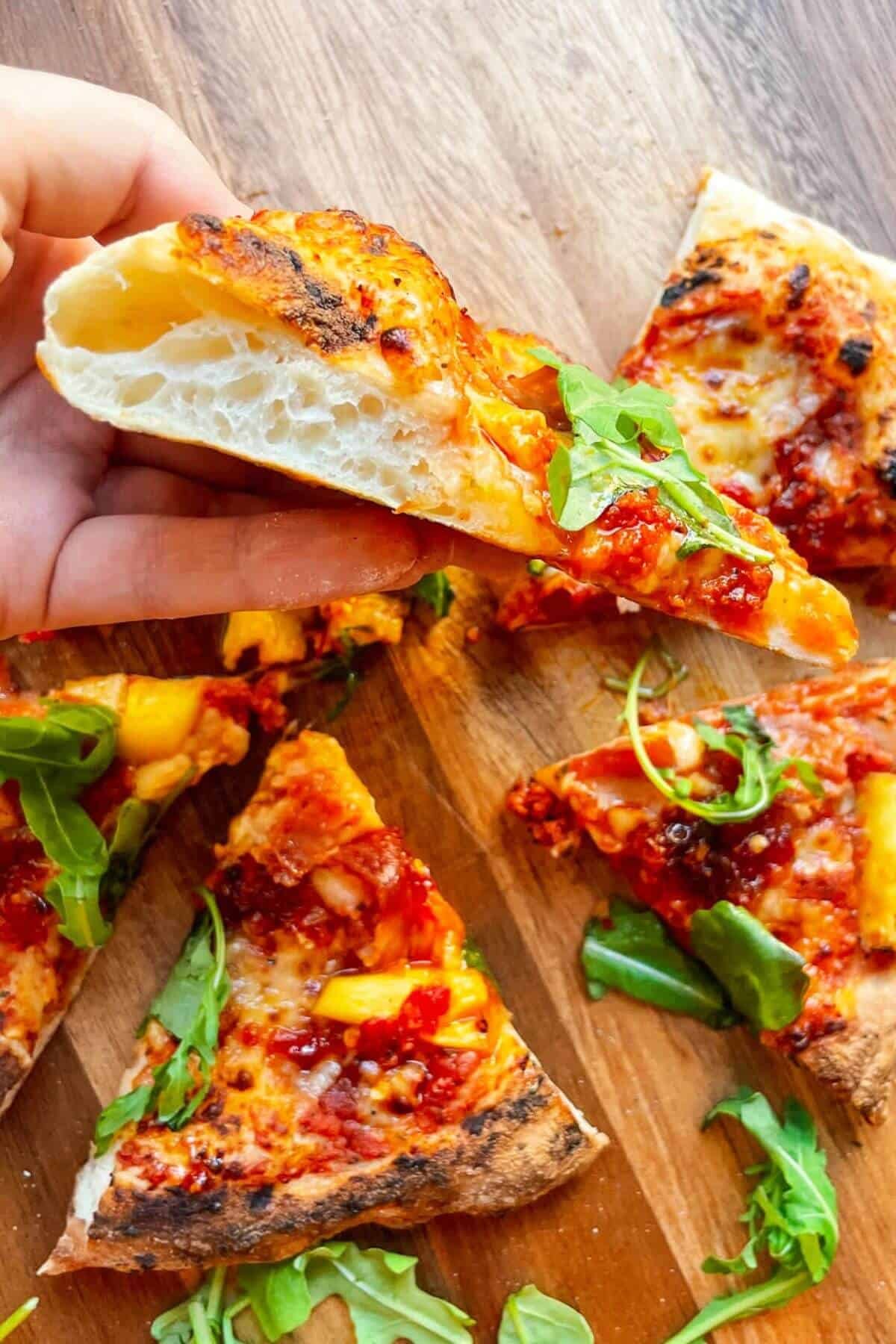 Hand holding piece of spicy Hawaiian pizza up to show cross section.