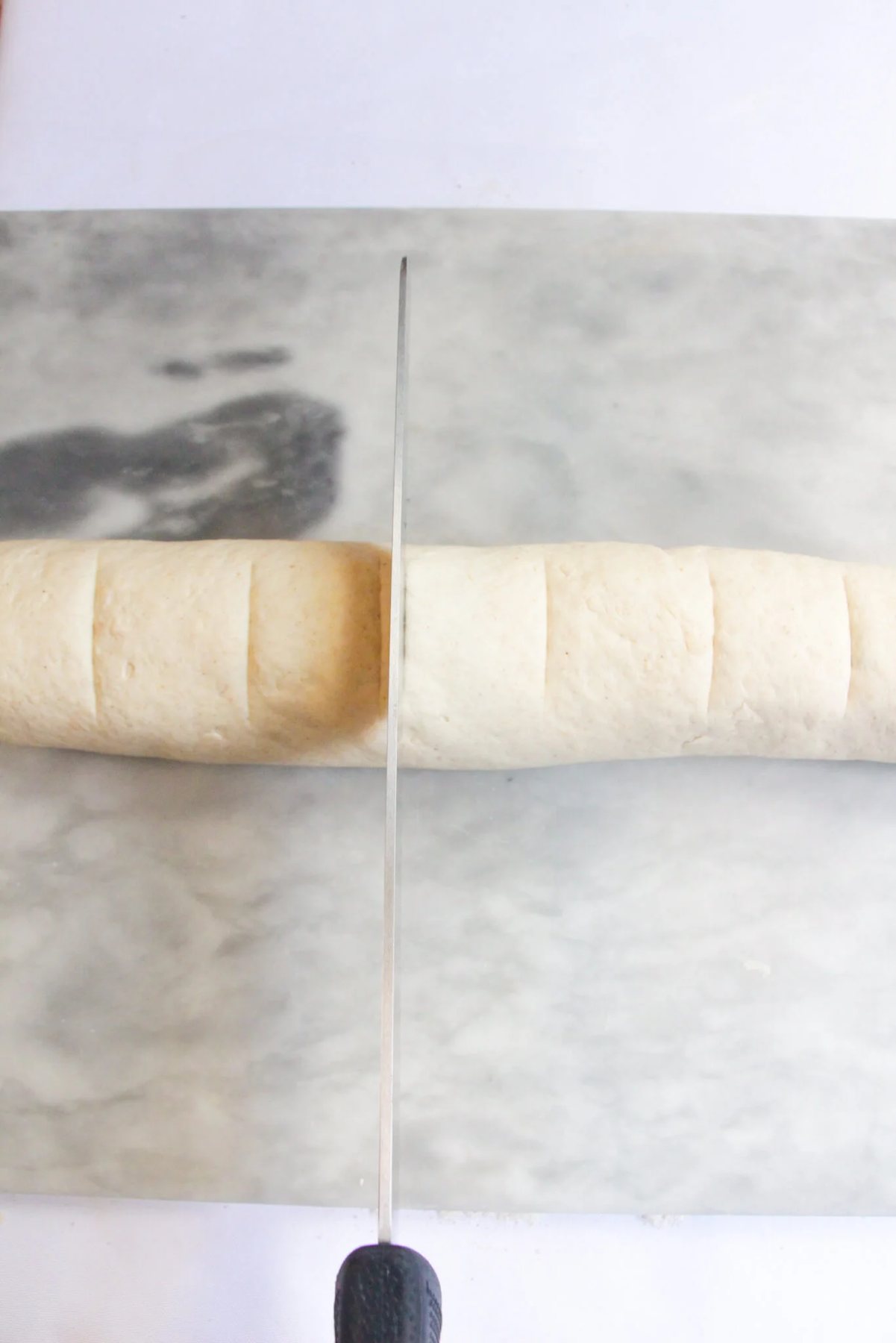 Large bread knife about to slice into a long rolled sausage shaped cinnamon bun.