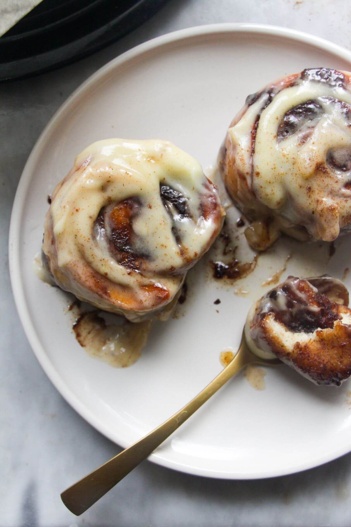Close up of 2 pumpkin spice cinnamon rolls on a white plate with a small spoon.
