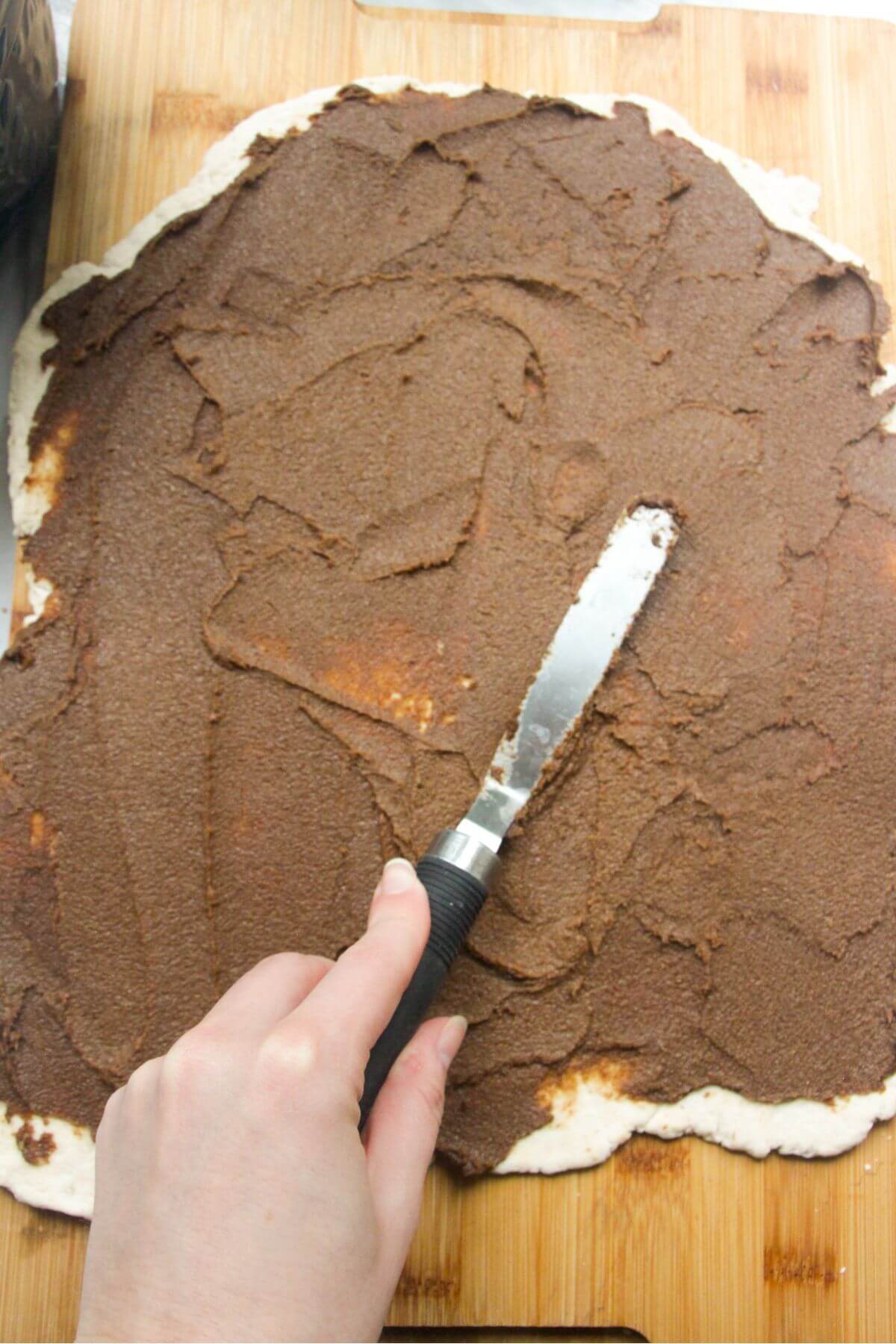 Spatula smoothing pumpkin spice sugar mix onto the rolled out dough.
