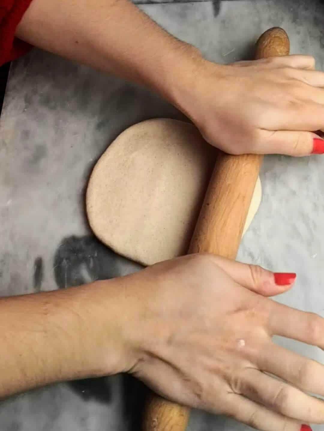 Hands continuing to roll out the easy soft flatbread dough into a circle.