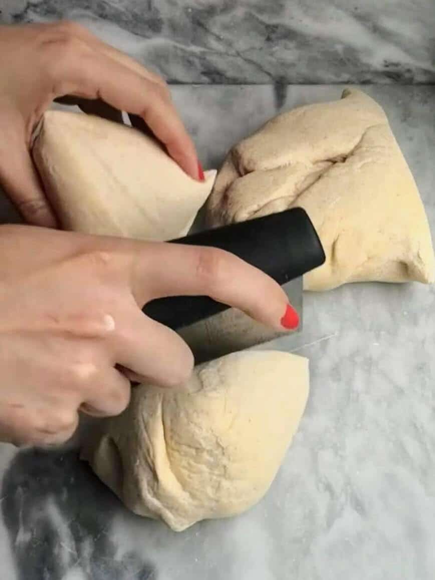 Hands chopping up the easy soft flatbread dough into eight pieces.