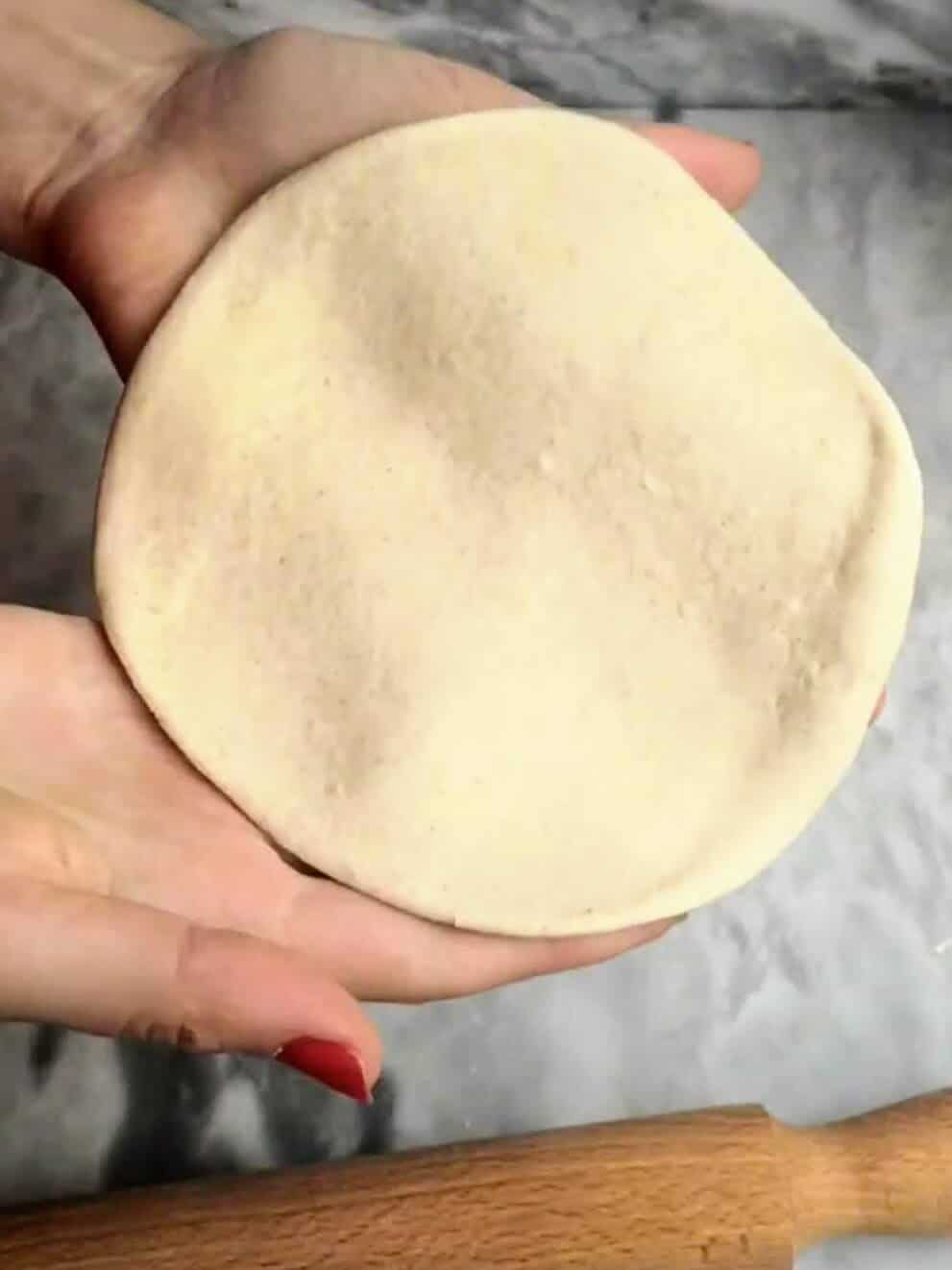 Hands holding up the easy soft flatbread ready for cooking.