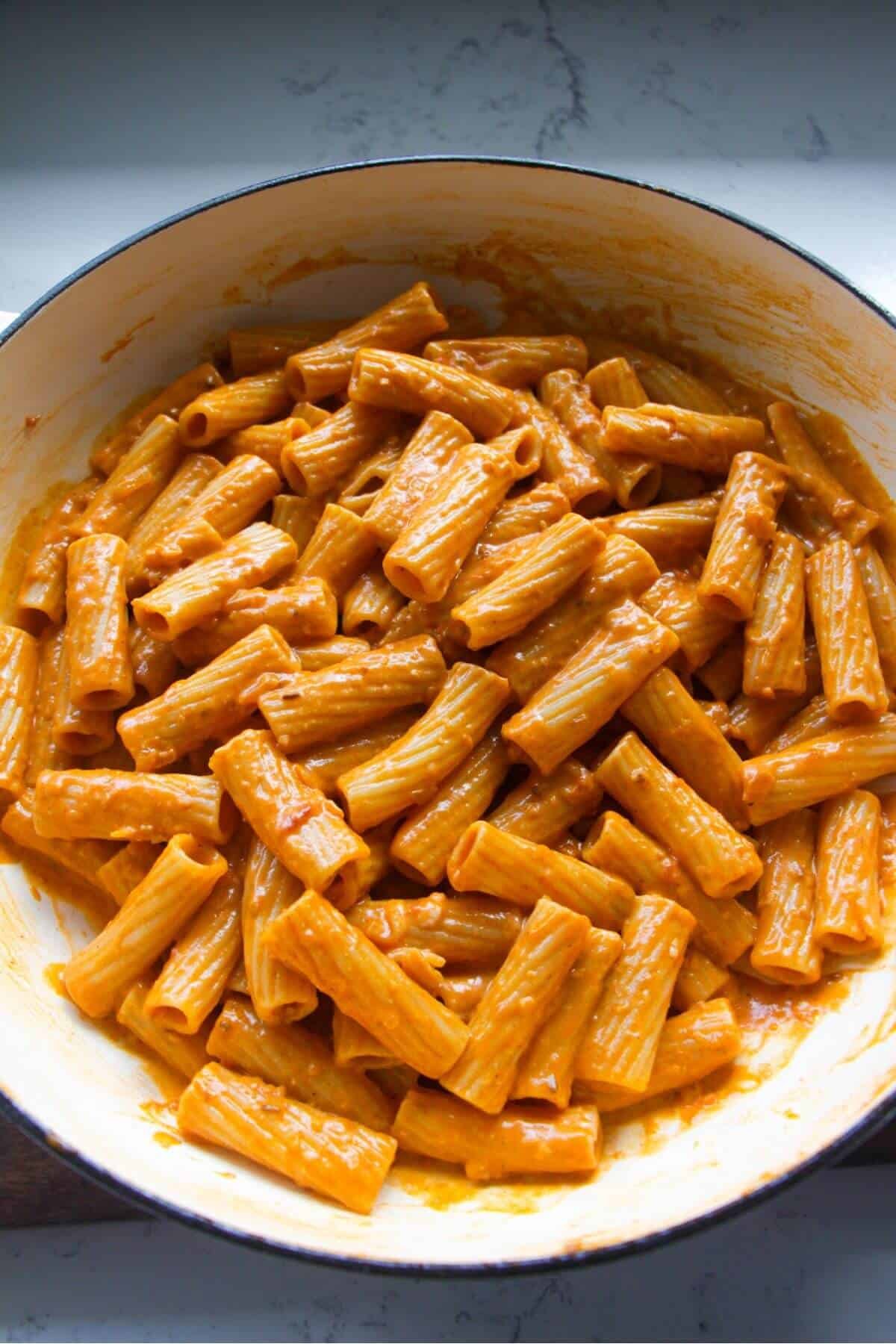 Rigatoni mixed through spicy tomato harissa sauce in a large white skillet.