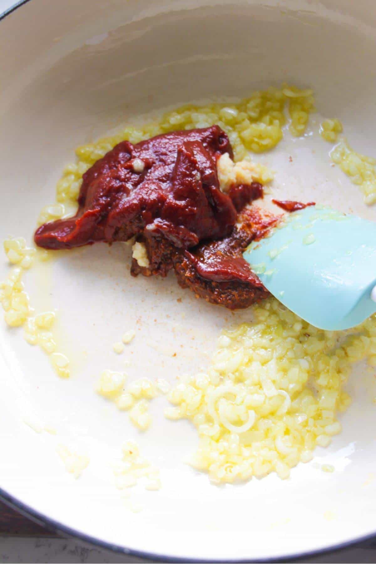 Adding tomato paste and harissa paste into a large white skillet.