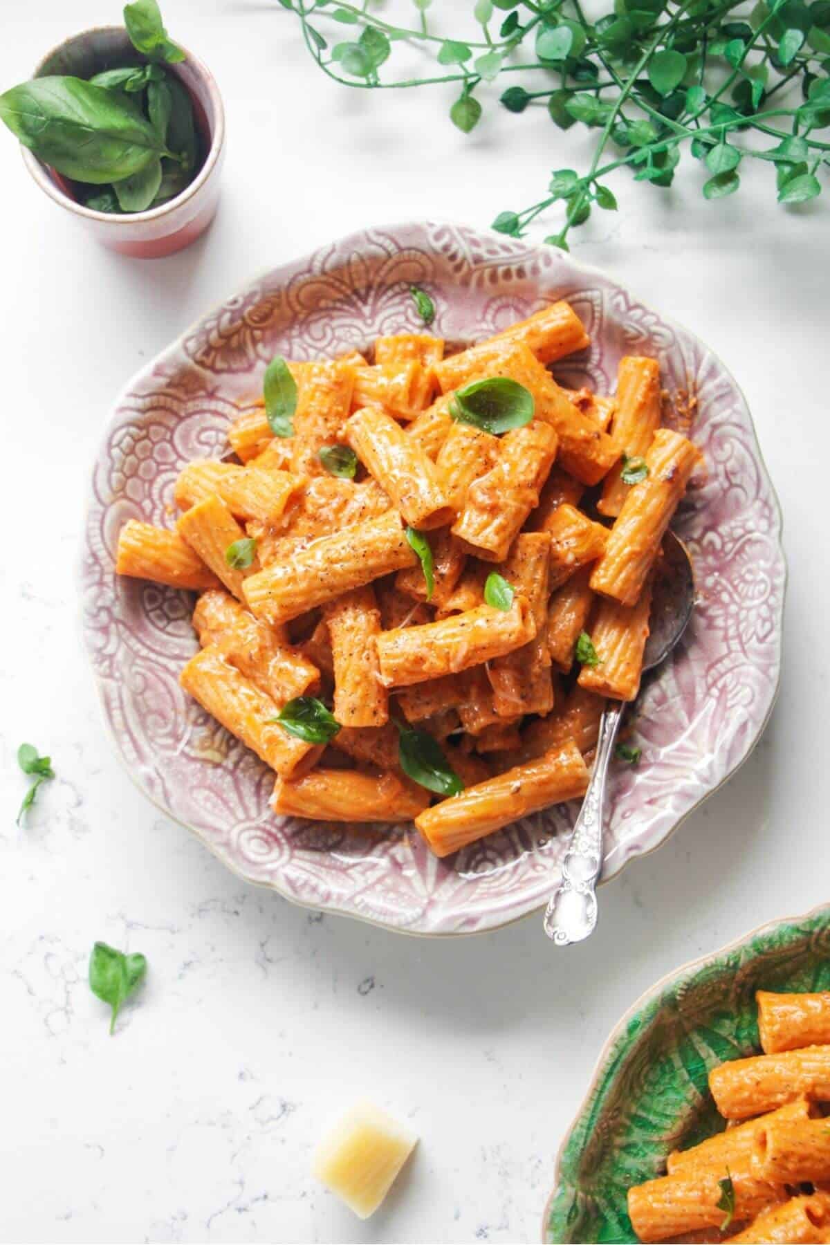 Spicy rigatoni on a pink plate with another small plate of rigatoni next to it.