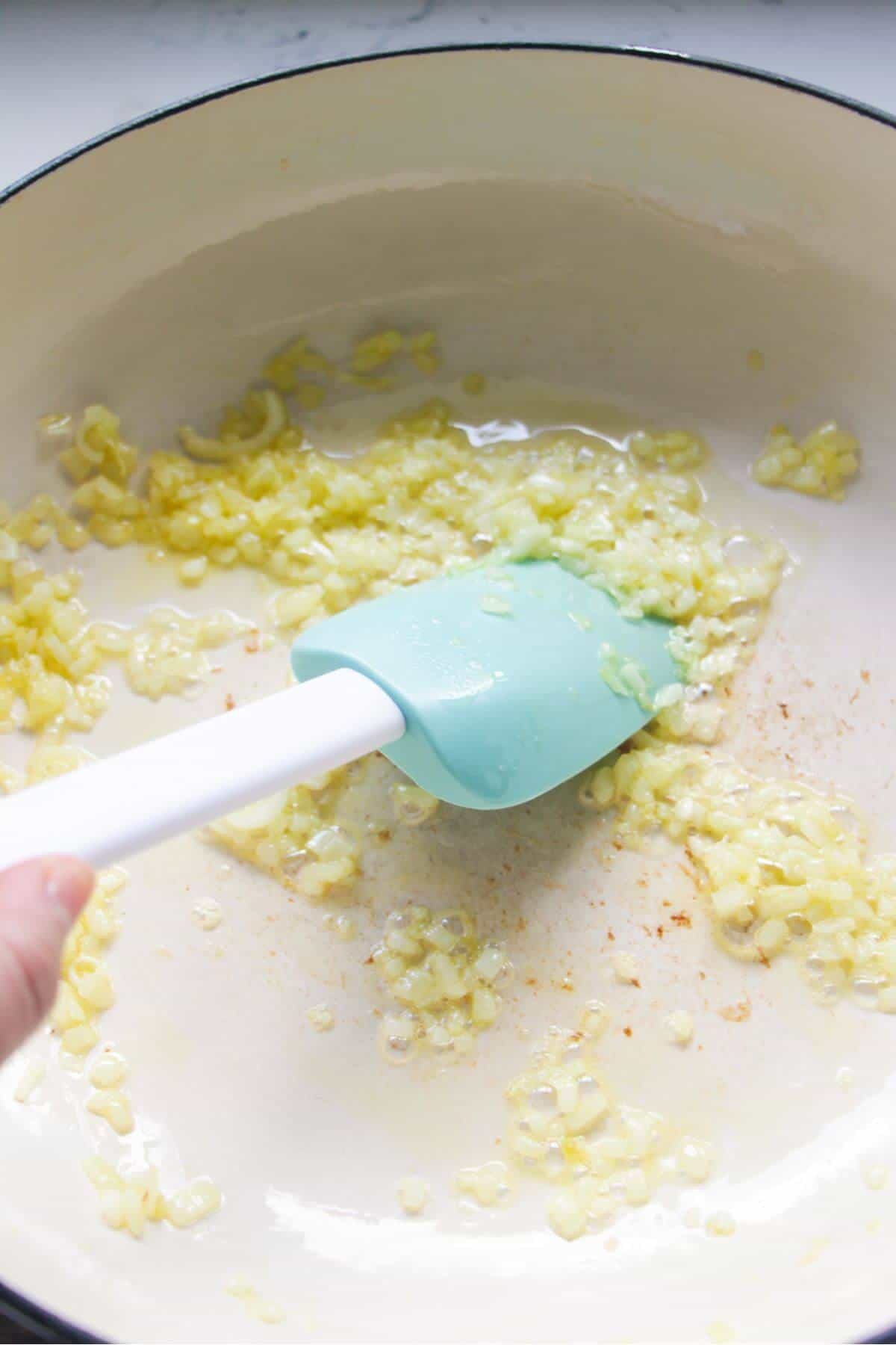 Stirring diced onion in a large white skillet.