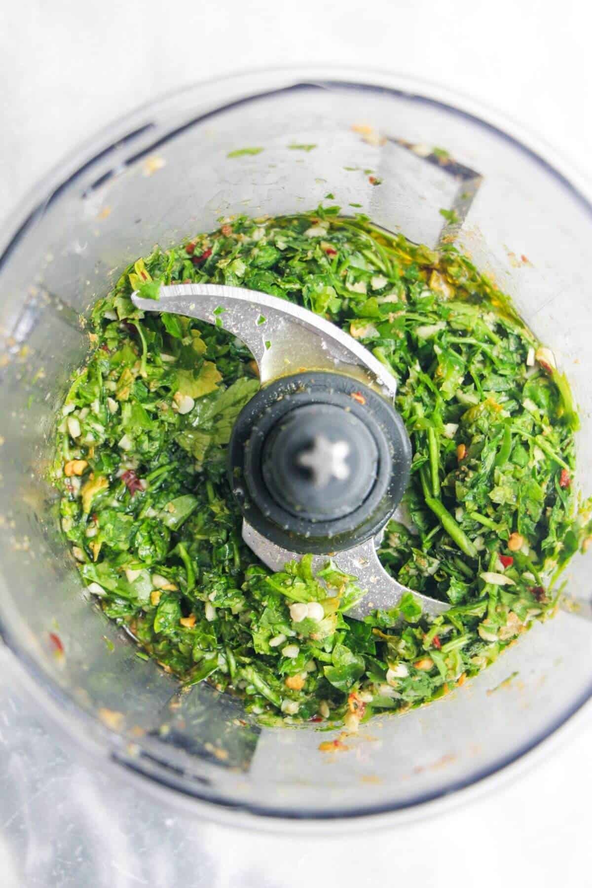 Olive oil added to zhoug sauce ingredients in a small food processor.