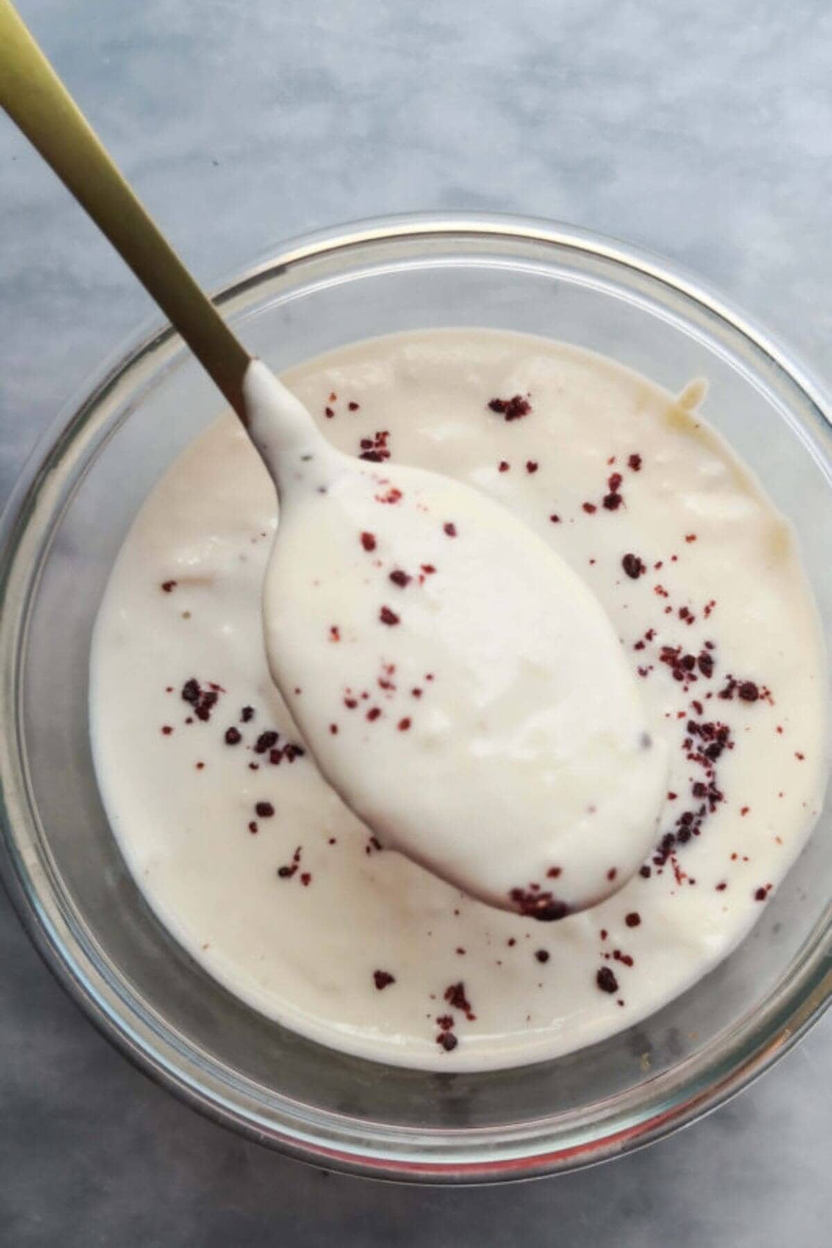 Yogurt tahini sauce in a small glass bowl with a gold spoon coming out of it .