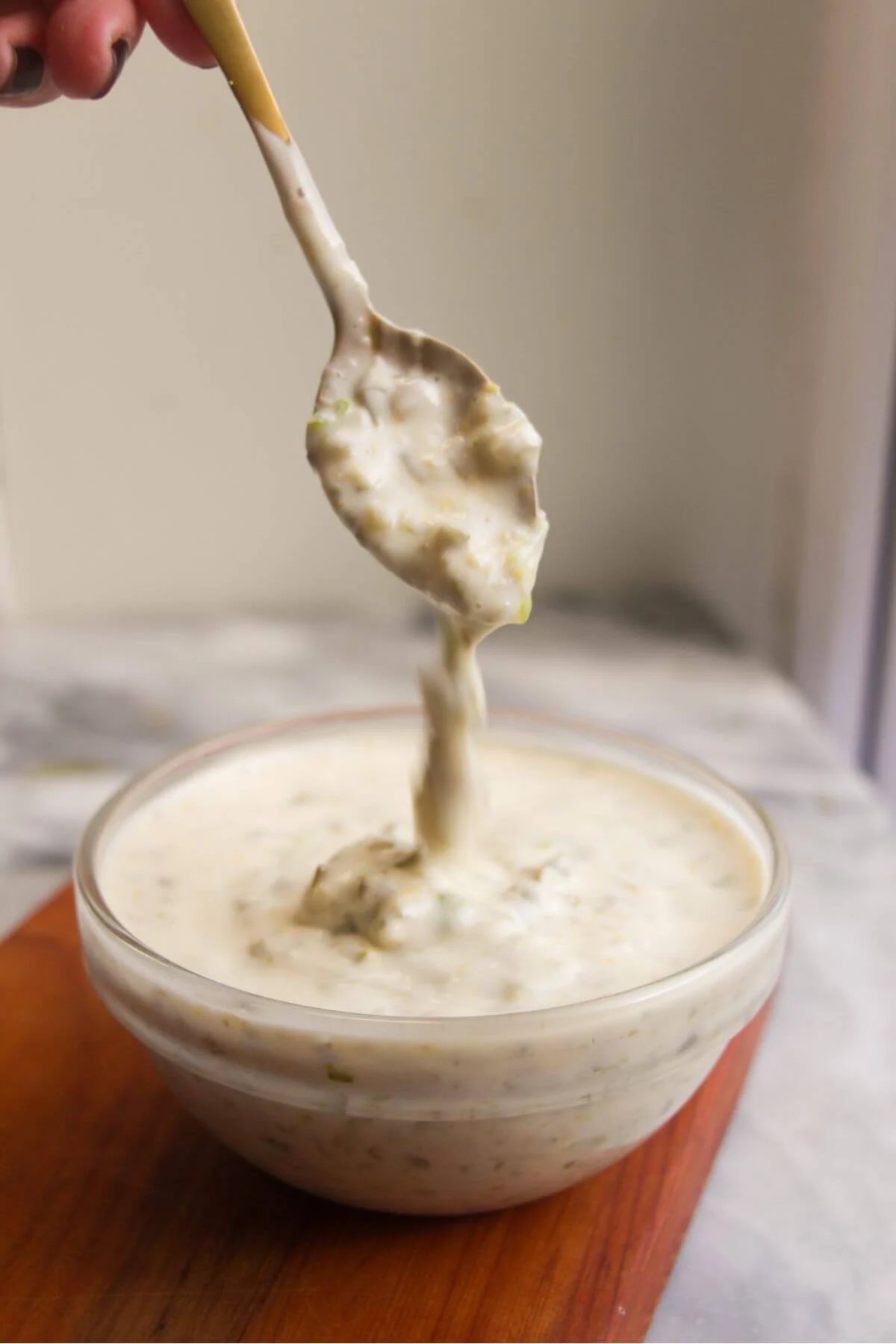Tartare sauce dripping off a small spoon into a glass bowl.
