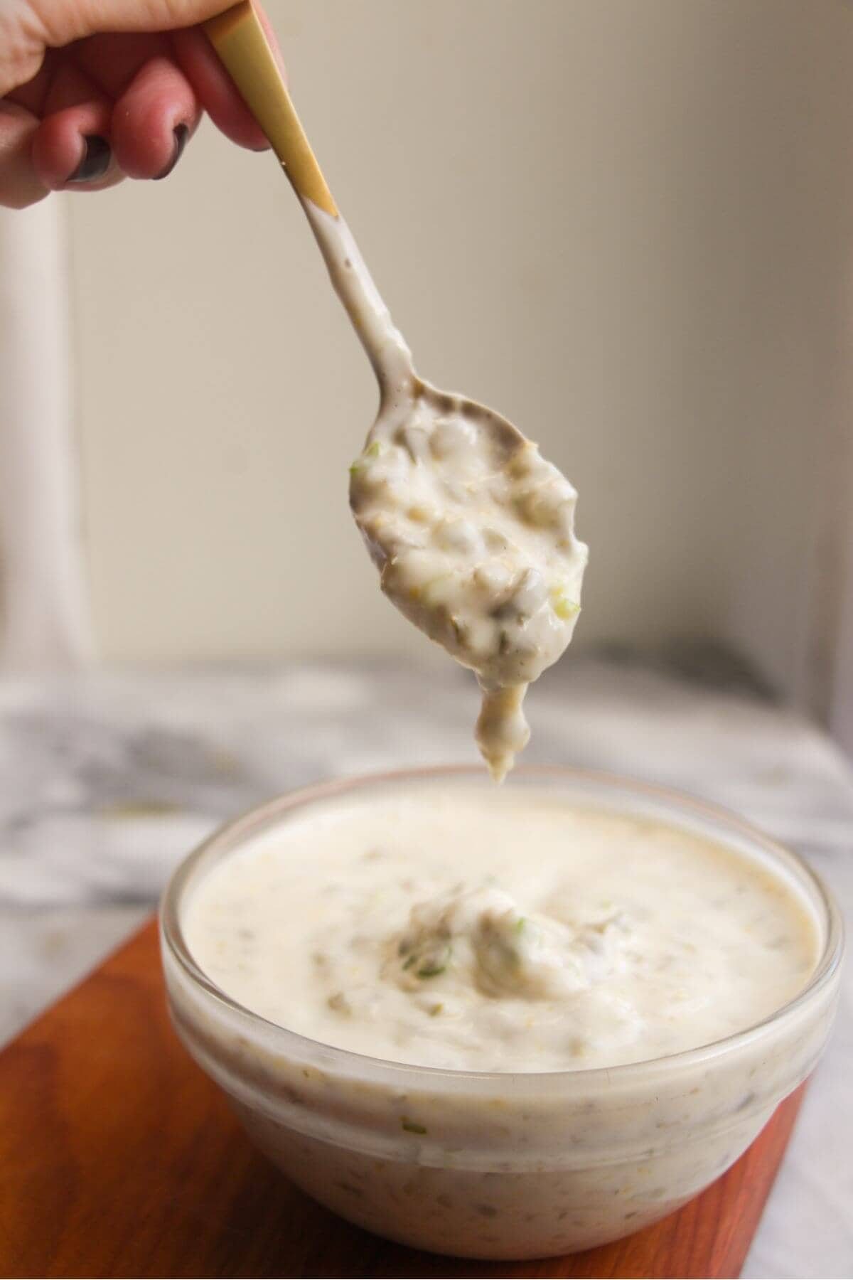 Tartare sauce dripping off a small spoon into a glass bowl.