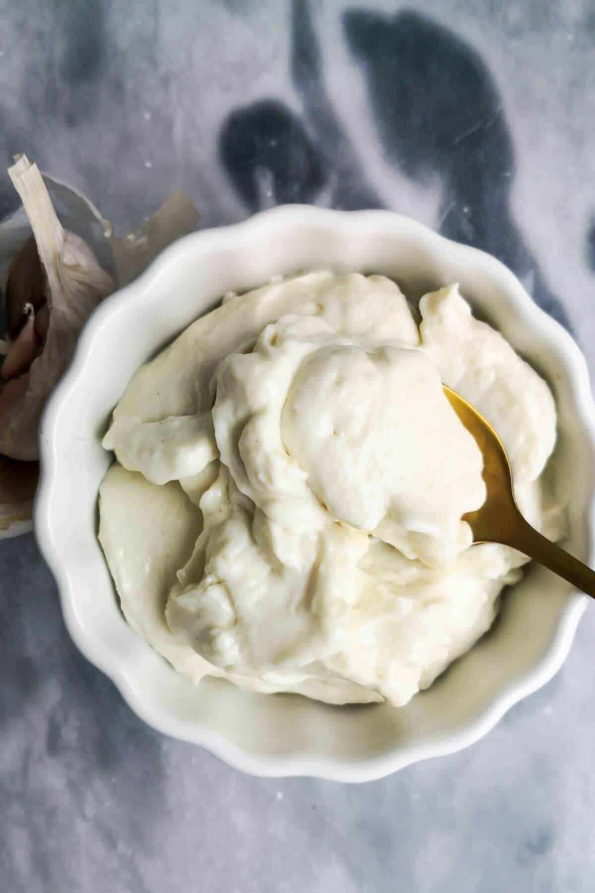 Small white bowl with vegan aioli, with a small gold spoon inside.
